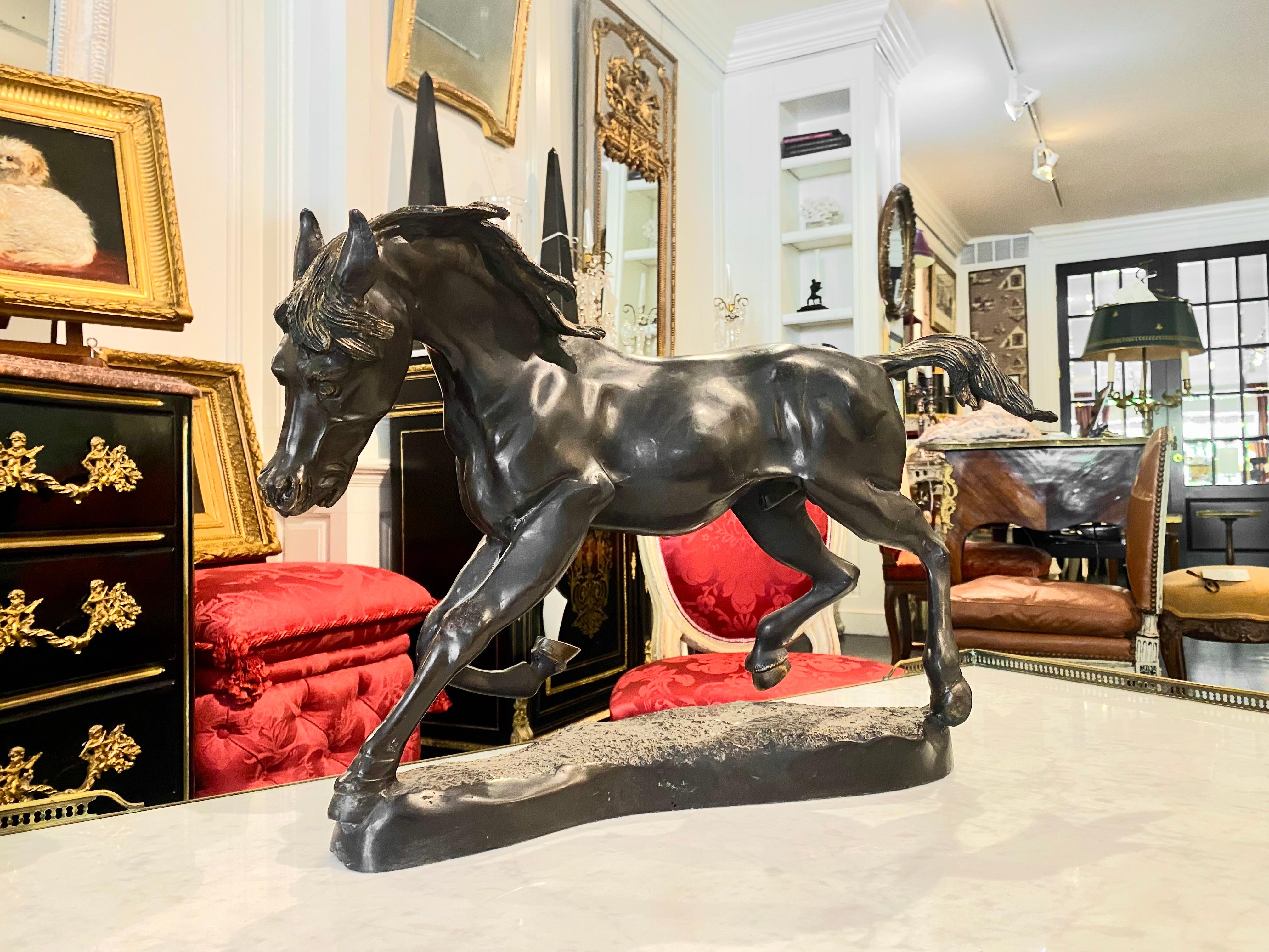 A majestic trotting horse cast in bronze. The wind blows through its mane and tail to create the striking impression that the horse is in movement. This sculpture is mounted on a rounded, textured base that emulates earth. The horse is meticulously