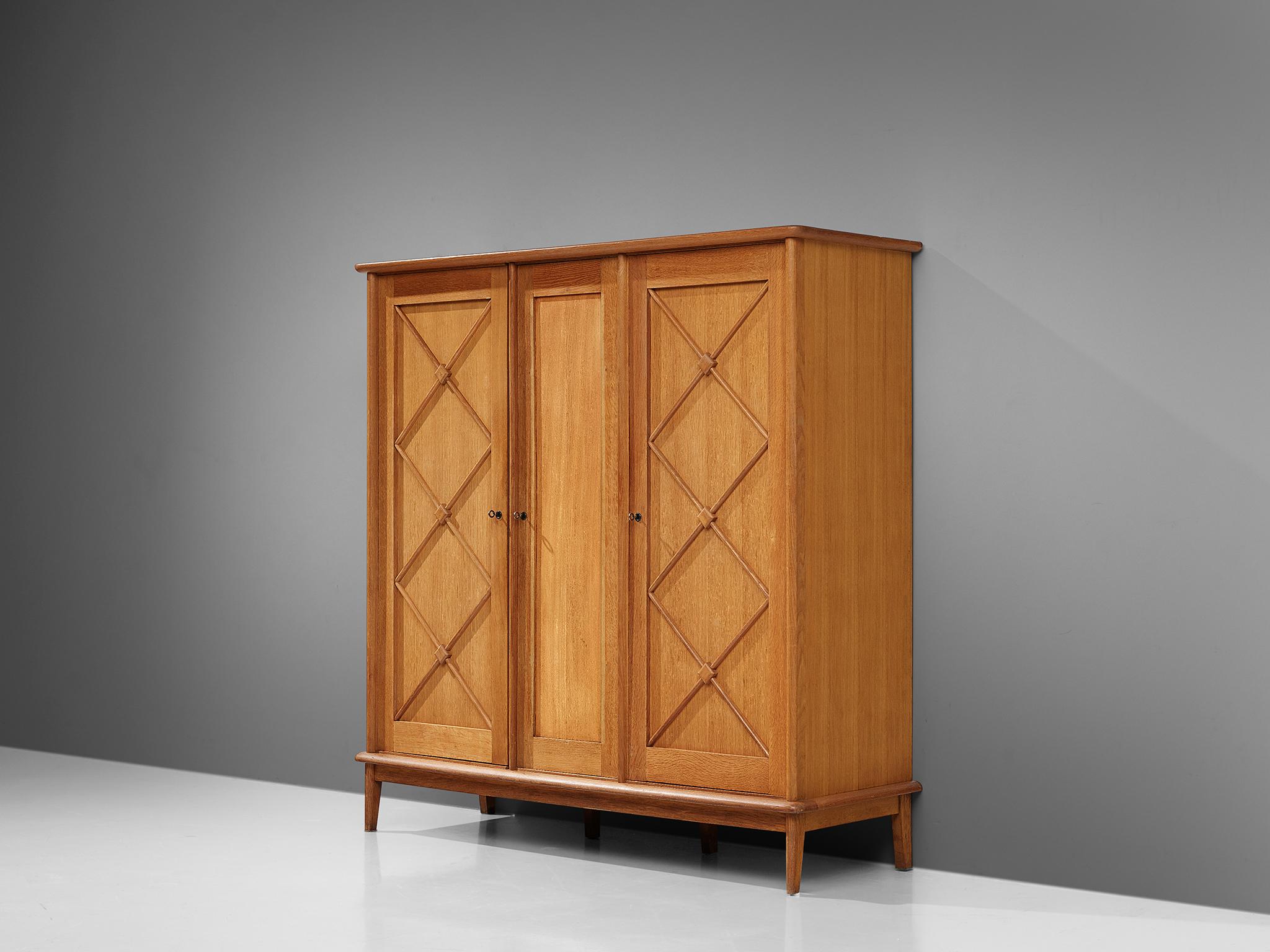 Large cabinet, oak, France, 1960s.

An elegant case piece in oak that features geometric details in the doors. The high board is lifted from the ground by slim, conical legs that give the solid looking body a more airy appearance. The cabinet