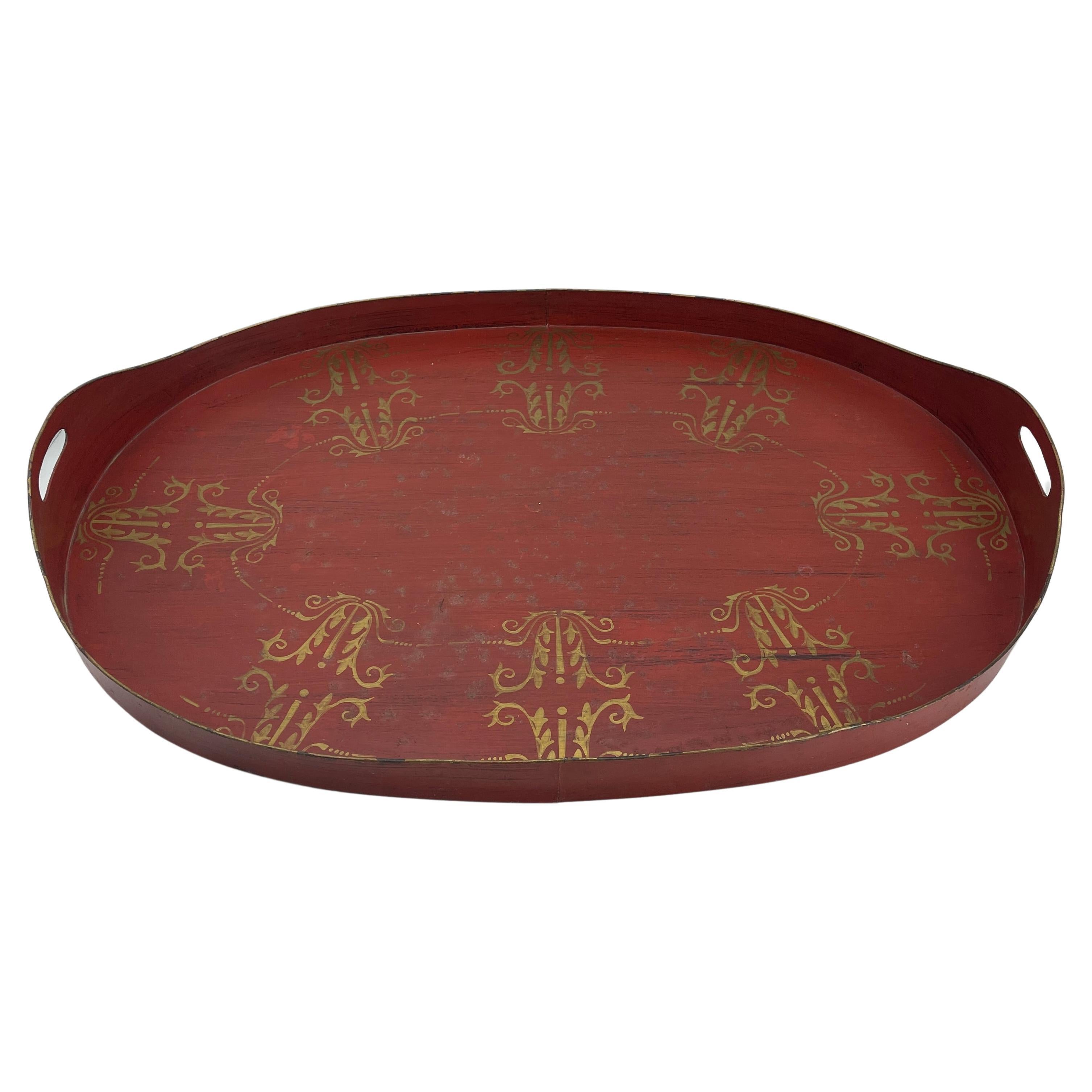 Hand-painted in the mid to late 19th century France, this red antique oval toleware tray with side handles features gold scroll patterns. This large impressive antique tray could be used on a coffee table or hang on a wall.