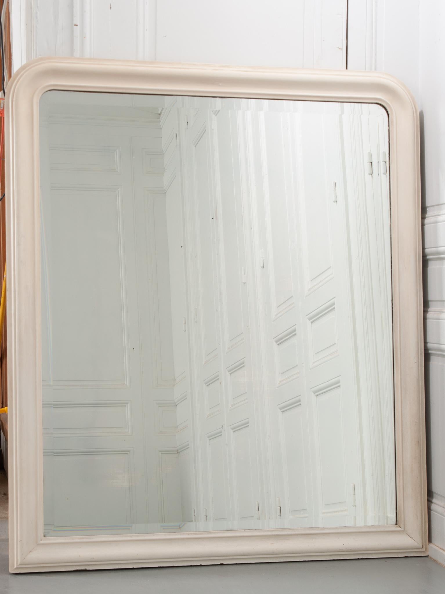 Dieser schlichte und raffinierte große Spiegel im Louis-Philippe-Stil stammt aus dem Frankreich des 19. Jahrhunderts. Der kürzlich lackierte, ecrufarbene Formrahmen ist mit leichten Schnitzereien und einer eleganten, abgeschrägten Spiegelplatte