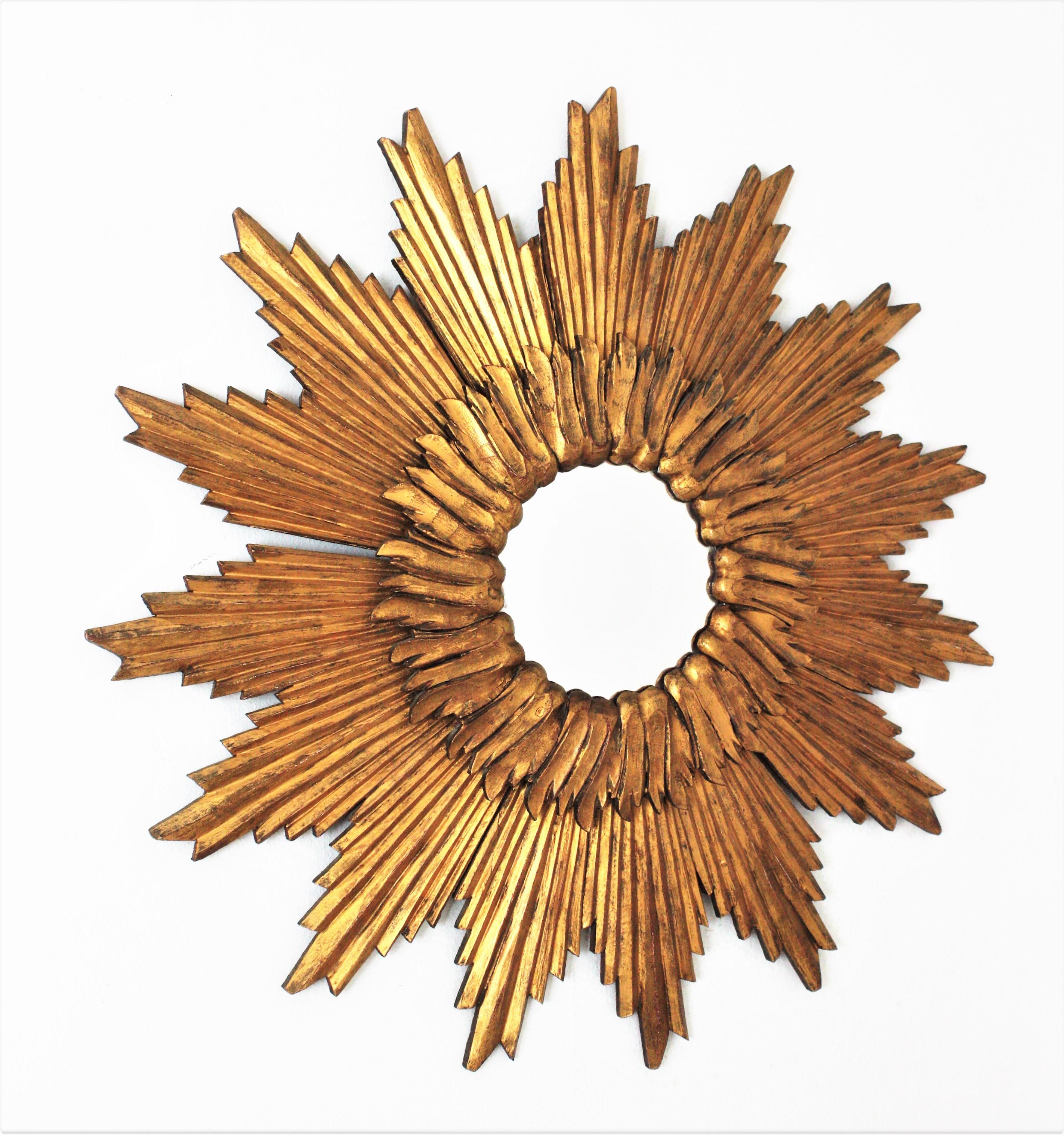 Eye-catching starburst sunburst convex mirror in gilt carved wood. France, 1960s.
The glass is framed by a circular layer of short beams and a large layer with giltwood beams with sunburst or starburst disposition. 
This glamourous mirror will be a