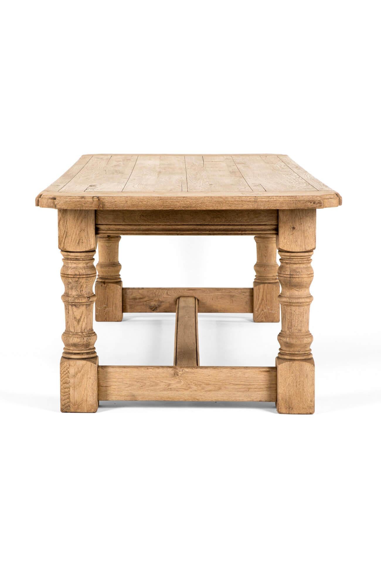 Une table de ferme imposante en chêne blanchi avec un plateau en planches épaisses.

Le plateau large et spacieux a des extrémités clivées et sculptées.

Le plateau est soutenu par des balustres tournés bien positionnés et unis par des châssis