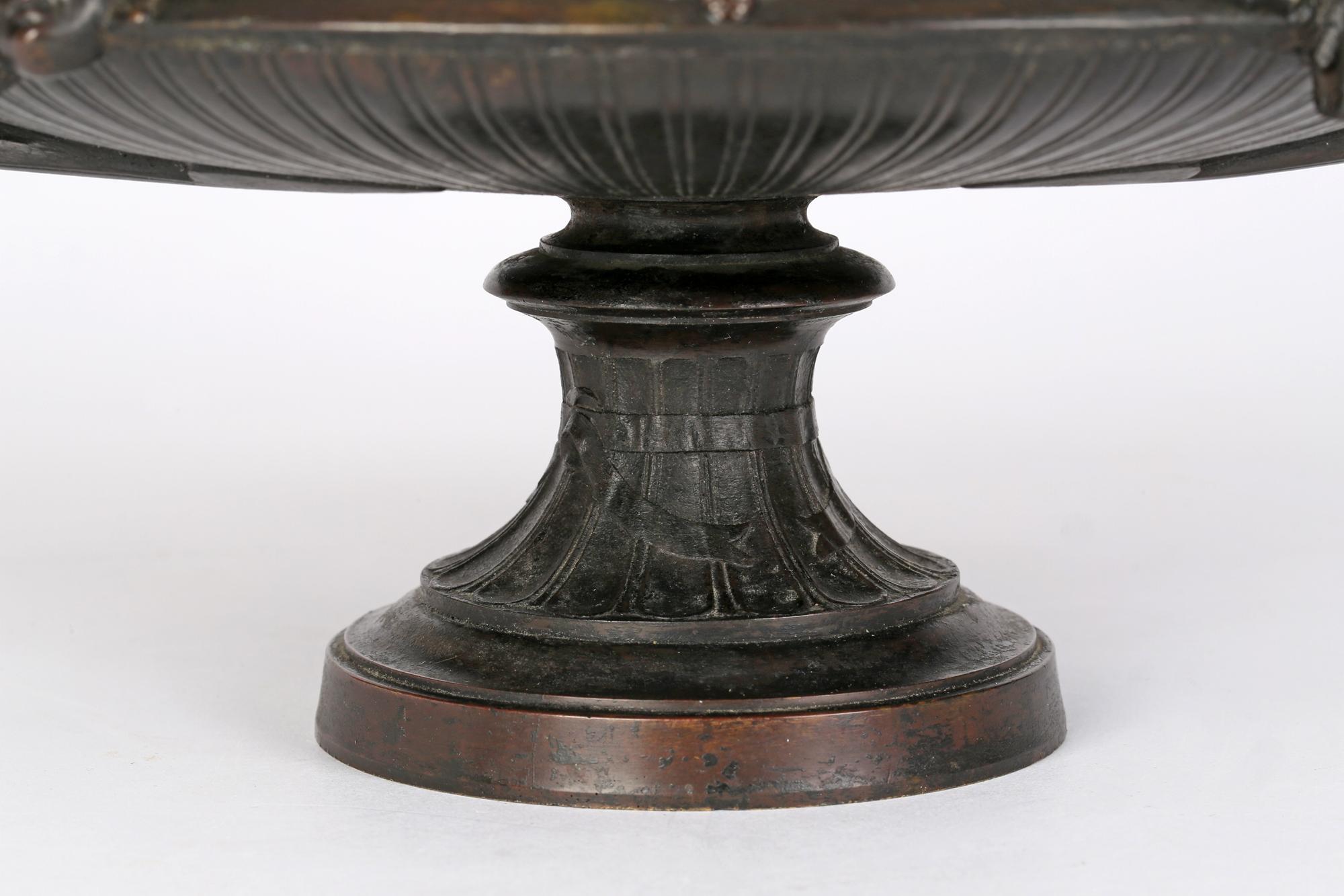 A large and impressive antique French (or possibly Italian Grand Tour) twin handled bronze tazza or shallow bowl decorated with masks dating from the 19th century. The large rounded tazza stands raised on a central column pedestal base and has a