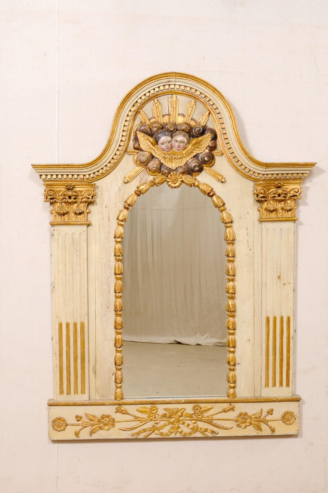 A French mirror with fabulous carvings and original paint & gilt from the turn of the 18th and 19th century. This antique mirror from France features an exaggerated arch pediment top with dentil molding beneath the top trim and pair of rosy-cheeked