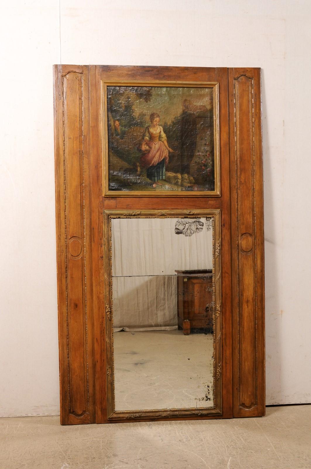 A tall French trumeau wood mirror, with oil painting framed atop, from the turn of the 18th and 19th century. This antique mirror from France, in the typical trumeau design, features a tall wooden surround with painting mounted atop a mirror below,