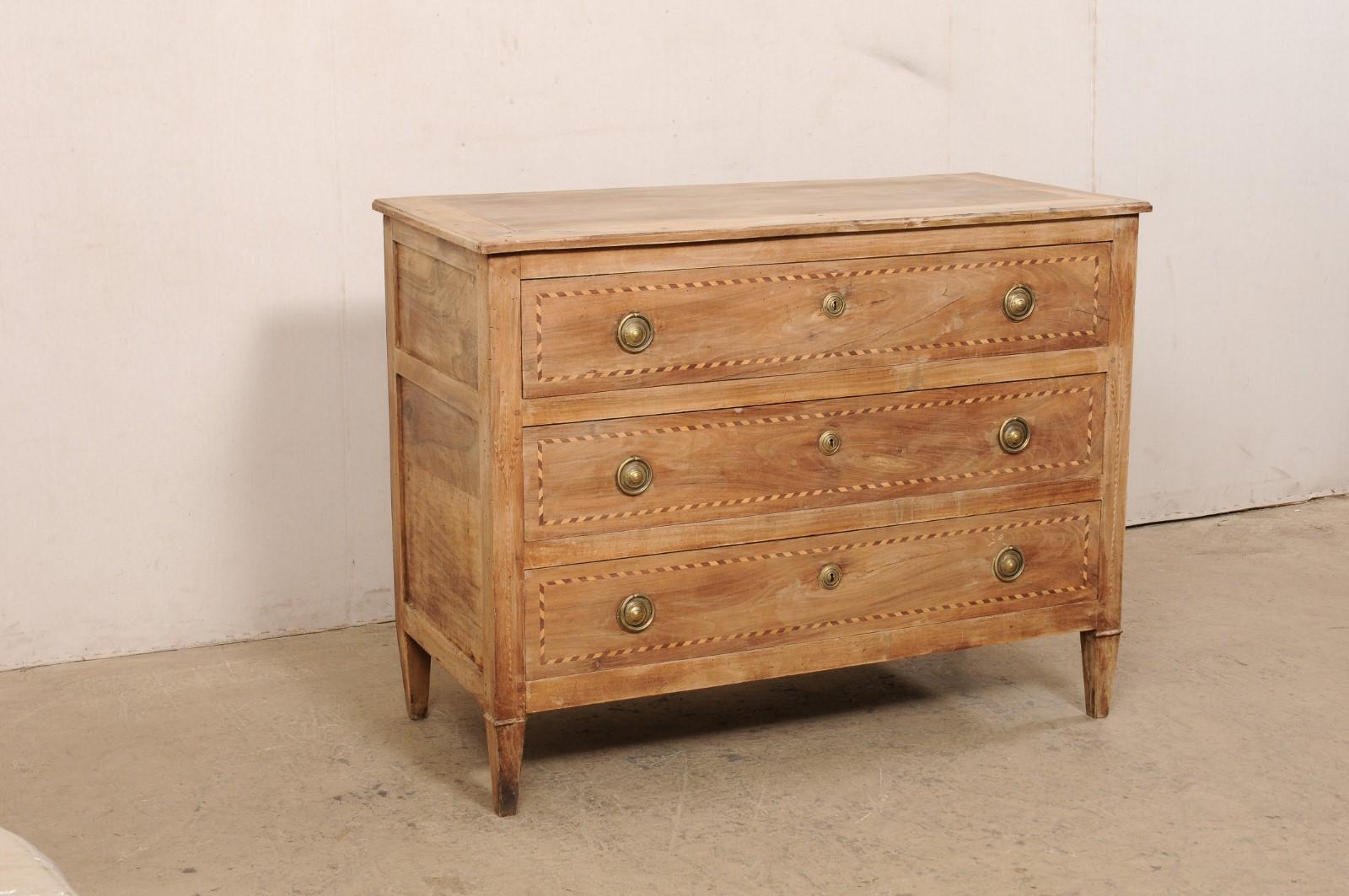 A French walnut commode from the turn of the 18th and 19th century. This antique chest from France houses three dove-tailed and graduated drawers, each nicely outlined with a ribbon style banding inlay and fitted with a pair of brass ring pulls