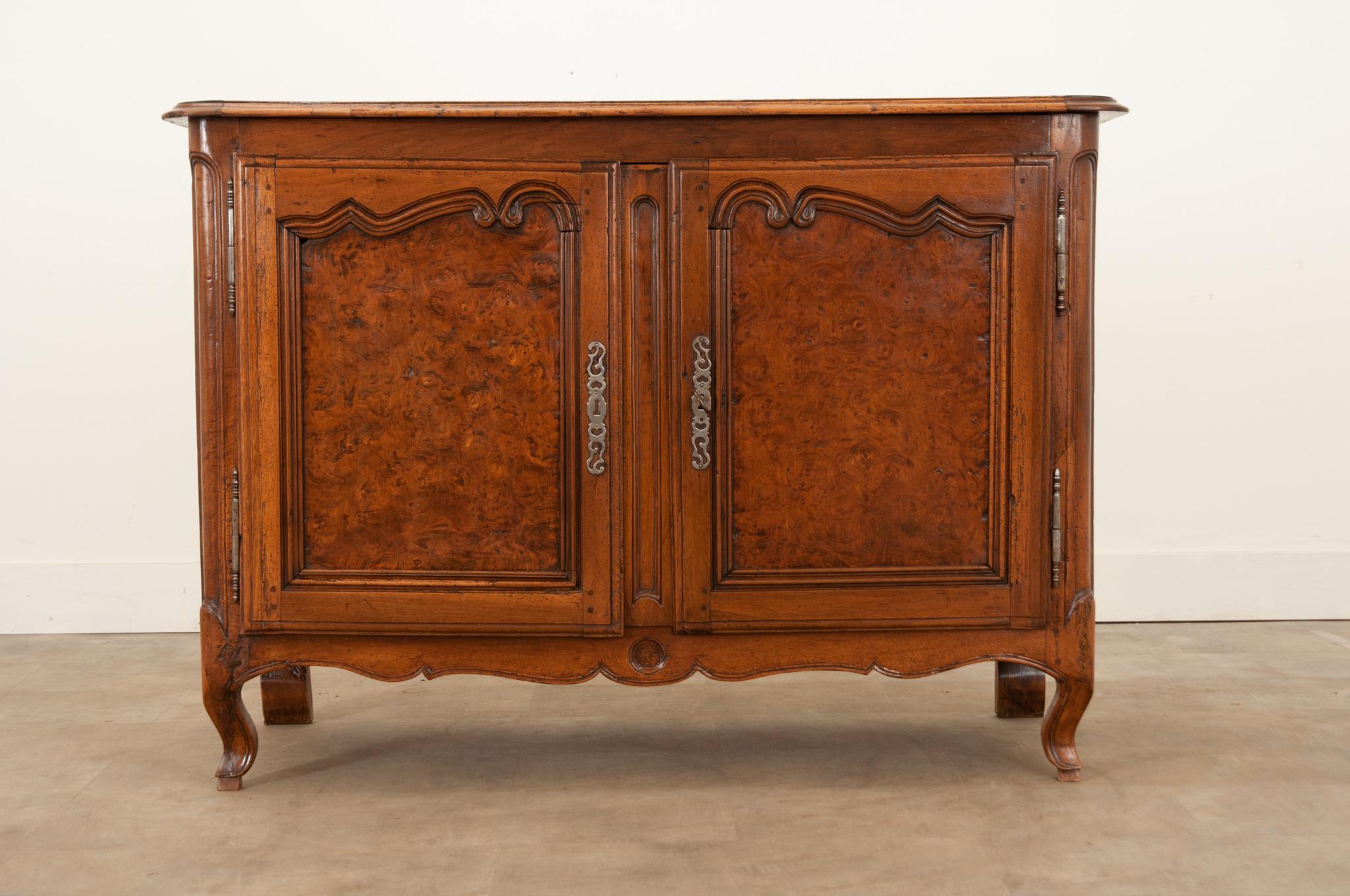 A beautiful solid walnut buffet, made in France circa 1790. The case antique is made with Provincial charm and style with burl walnut panels set into the shapely carved doors. These doors are hung with steel barrel hinges and can be secured with its