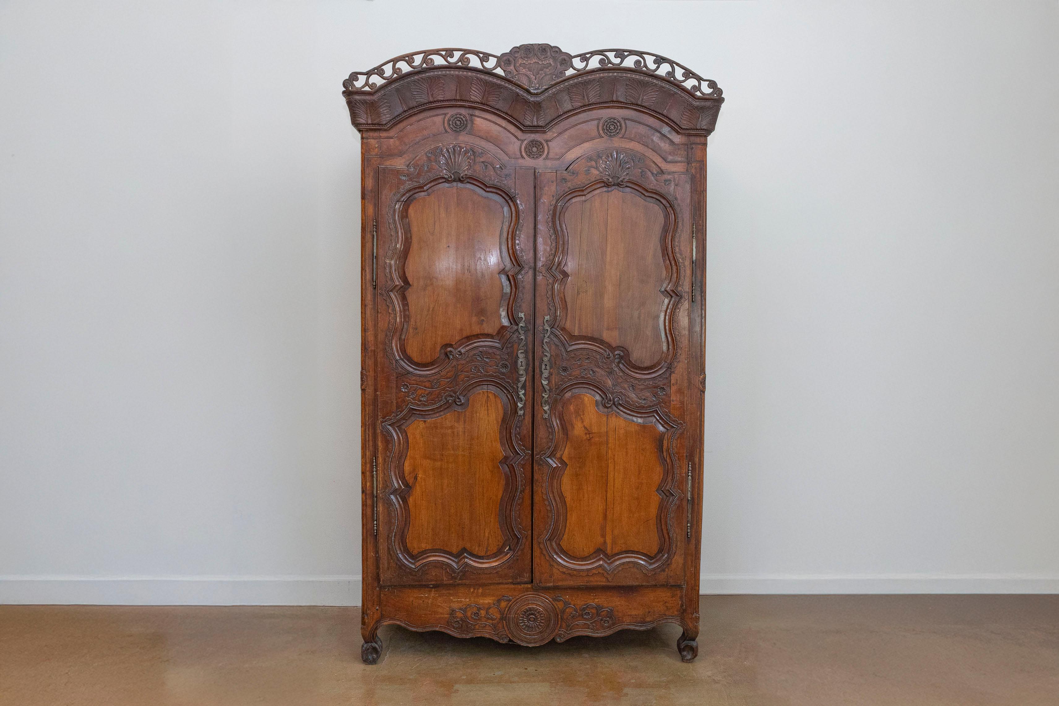A French late 18th century cherry armoire from Rennes with pierced cornice, floral and shell motifs. Born in the capital of the eastern region of Brittany, this French cherry armoire features a striking double arched cornice adorned with delicate