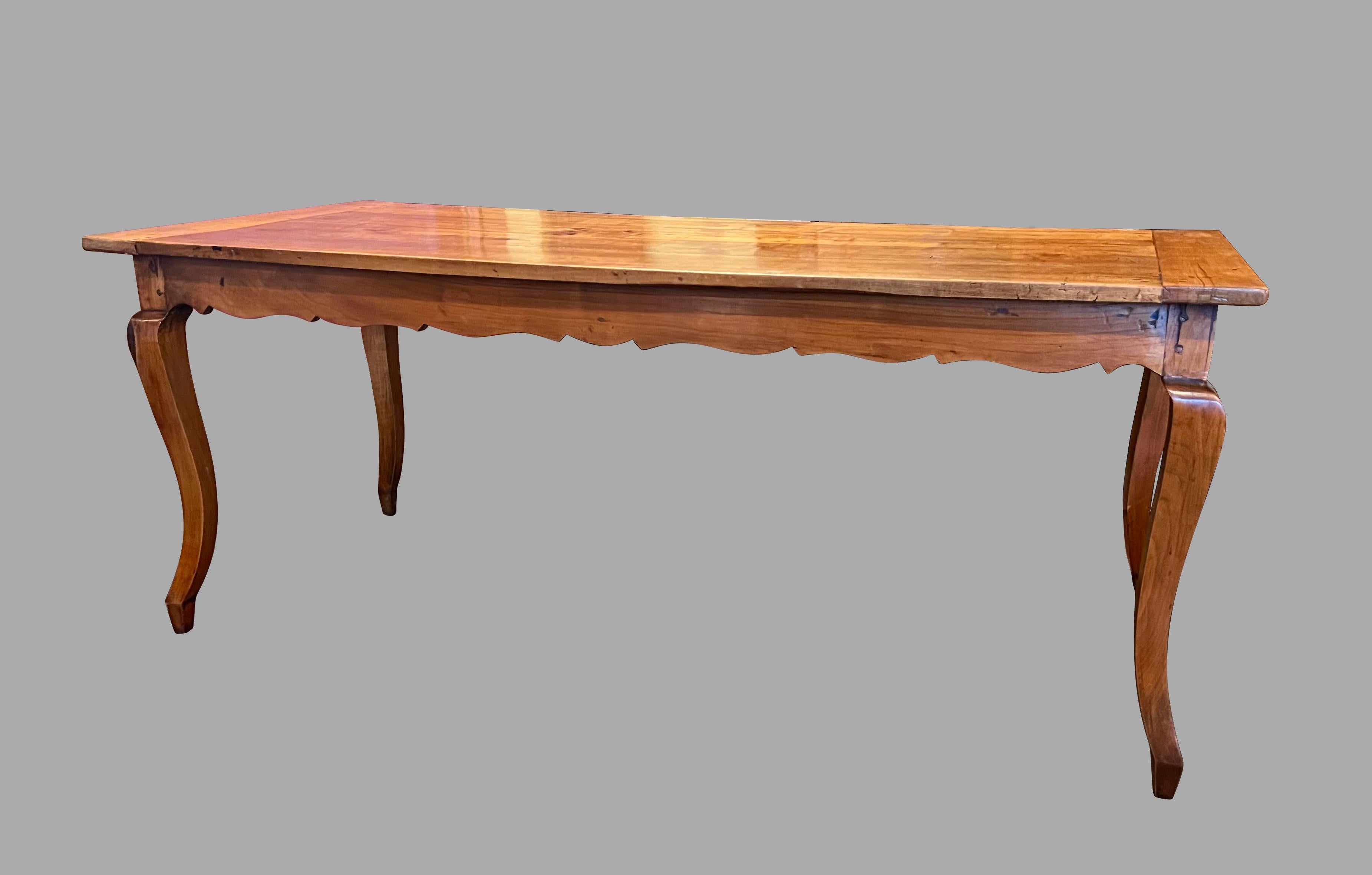 Atractiva mesa de granja francesa de madera de frutal, probablemente cerezo, con tablero de tablones sobre un delantal festoneado, un extremo con un cajón y el otro con una tabla de pan oculta, todo ello apoyado sobre elegantes patas cabriolé. La