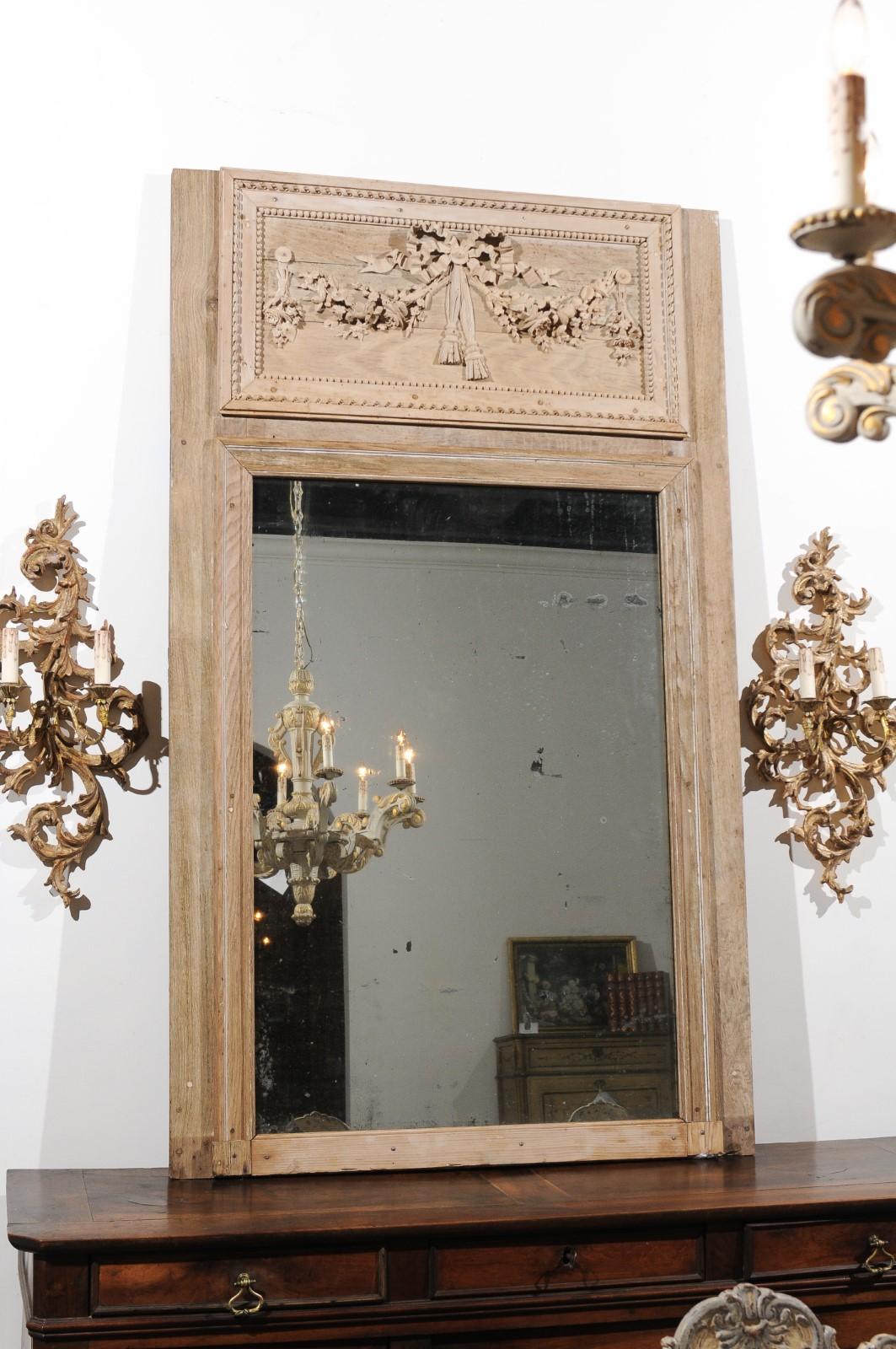 A French Louis XVI period carved wooden trumeau mirror from the late 18th century, with ribbon-tied garland of flowers and twisted motifs. Born in the later years of the 18th century, this exquisite wooden trumeau mirror features in its upper