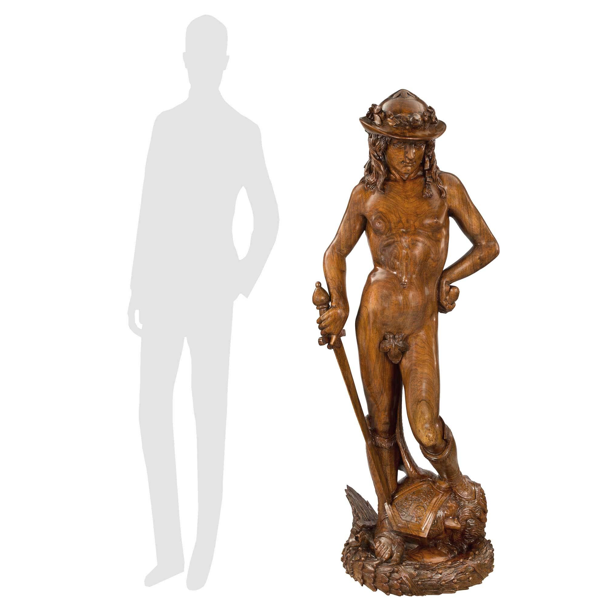 A striking and most impressive French late 18th early 19th century solid walnut of David having slain Goliath signed A. Mercié. The statue is raised by a finely carved wrap-around berried laurel band where David stands. The handsome David wears