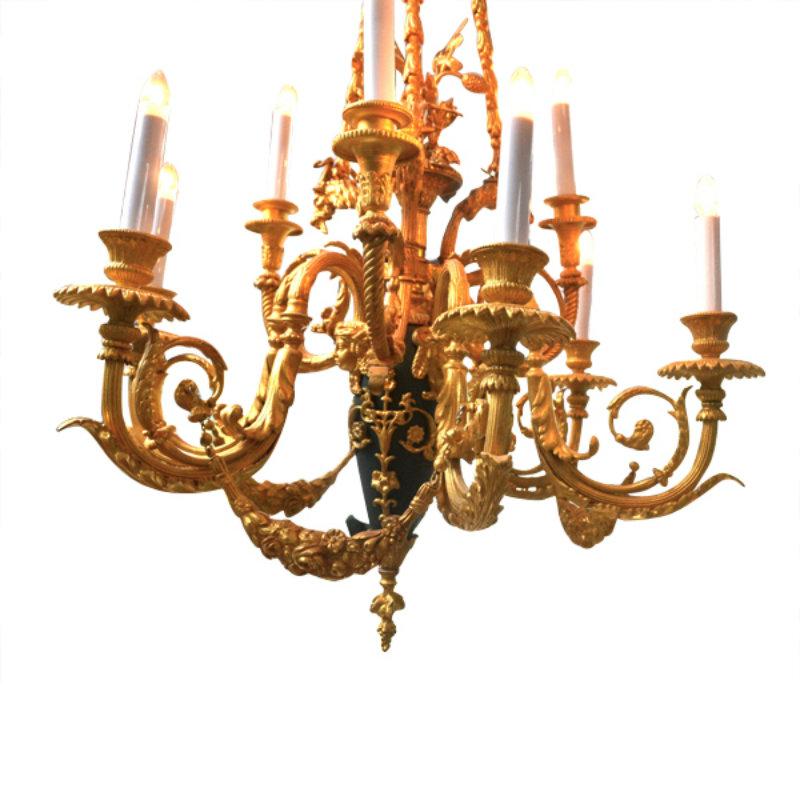 A gilt and patinated bronze chandelier very much in the Louis XVI style; three gilt chains hang from a draped canopy and connect with three goats heads which hold the upper three scrolling candle arms. In the middle of the upper arms is a gilded