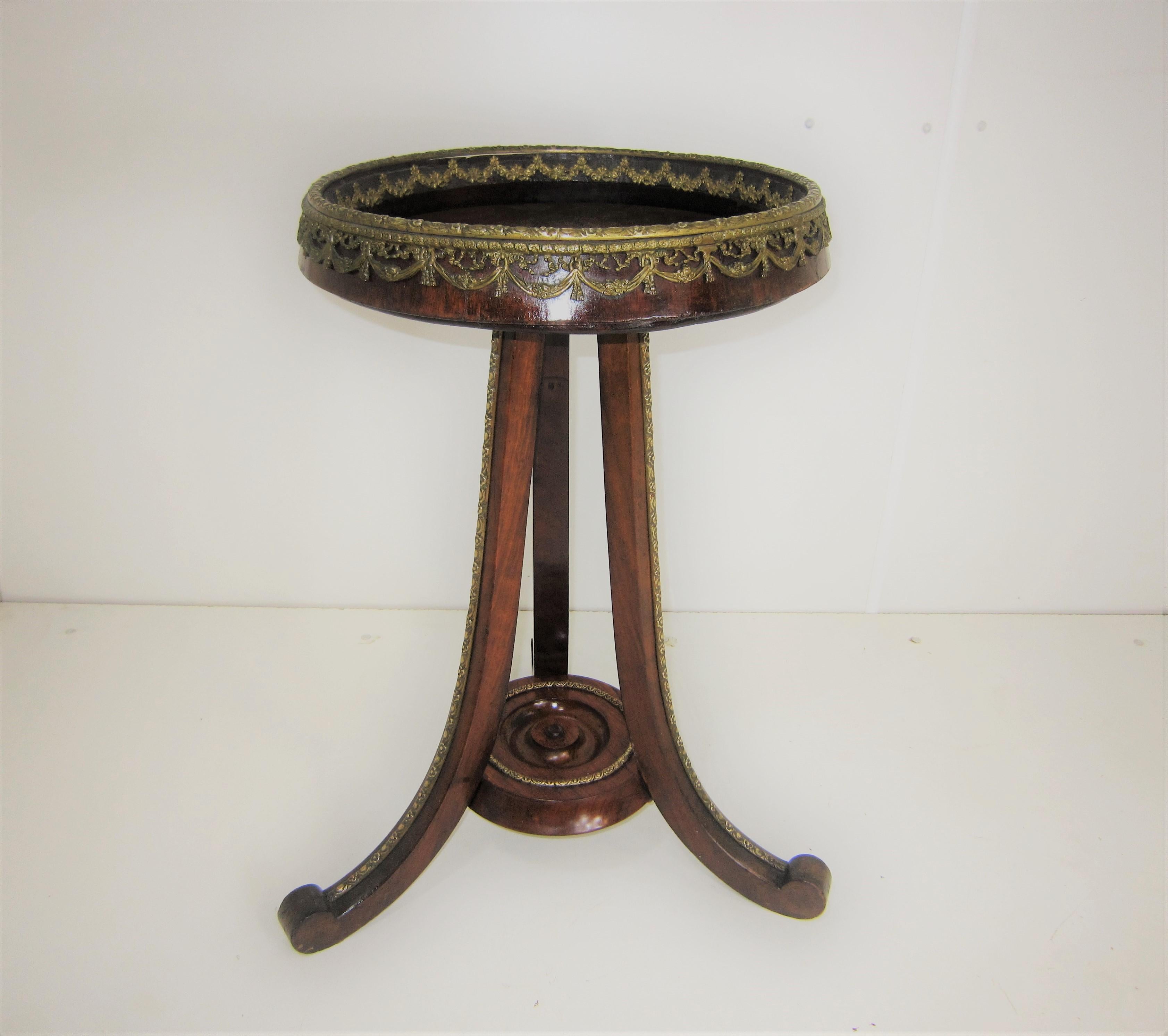 Antique walnut and fruitwood pedestal table with circular top featuring a gallery surround of foliate swag and floral motif ending in tripodal splay leg base. The bronze border is festooned on the inner as well as the outer top rim which gives the