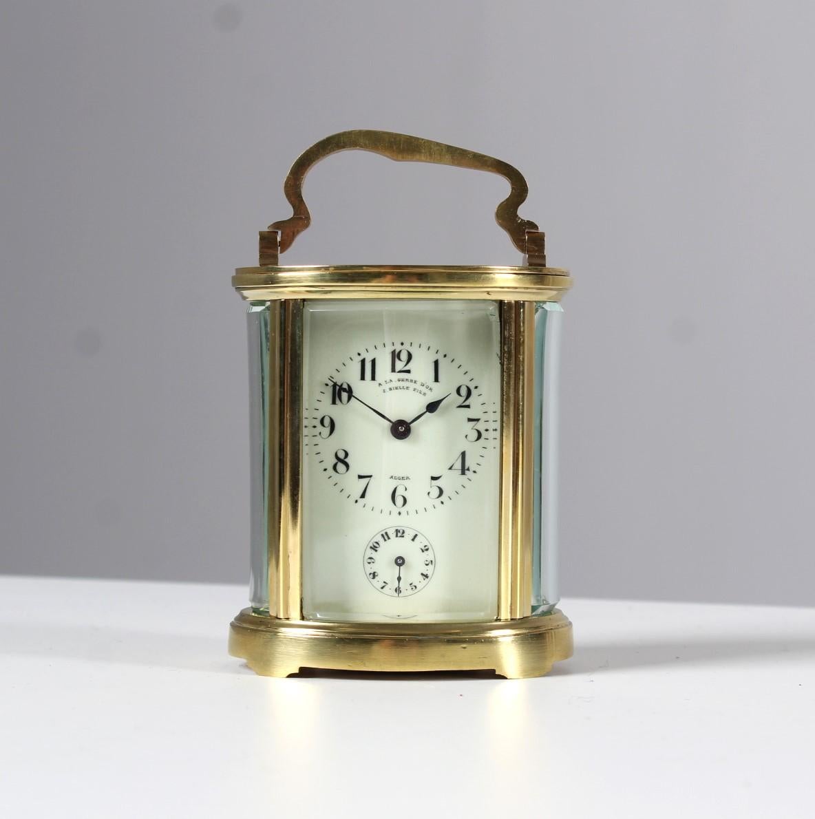 Antique travelling clock with alarm function from the late 19th century.
Measures: H x W x D: 12 (with handle 15) x 9.5 x 7 cm.

Oval brass case, glazed on all sides. Echappement visible from above.
Front enamel dial with black Arabic numerals