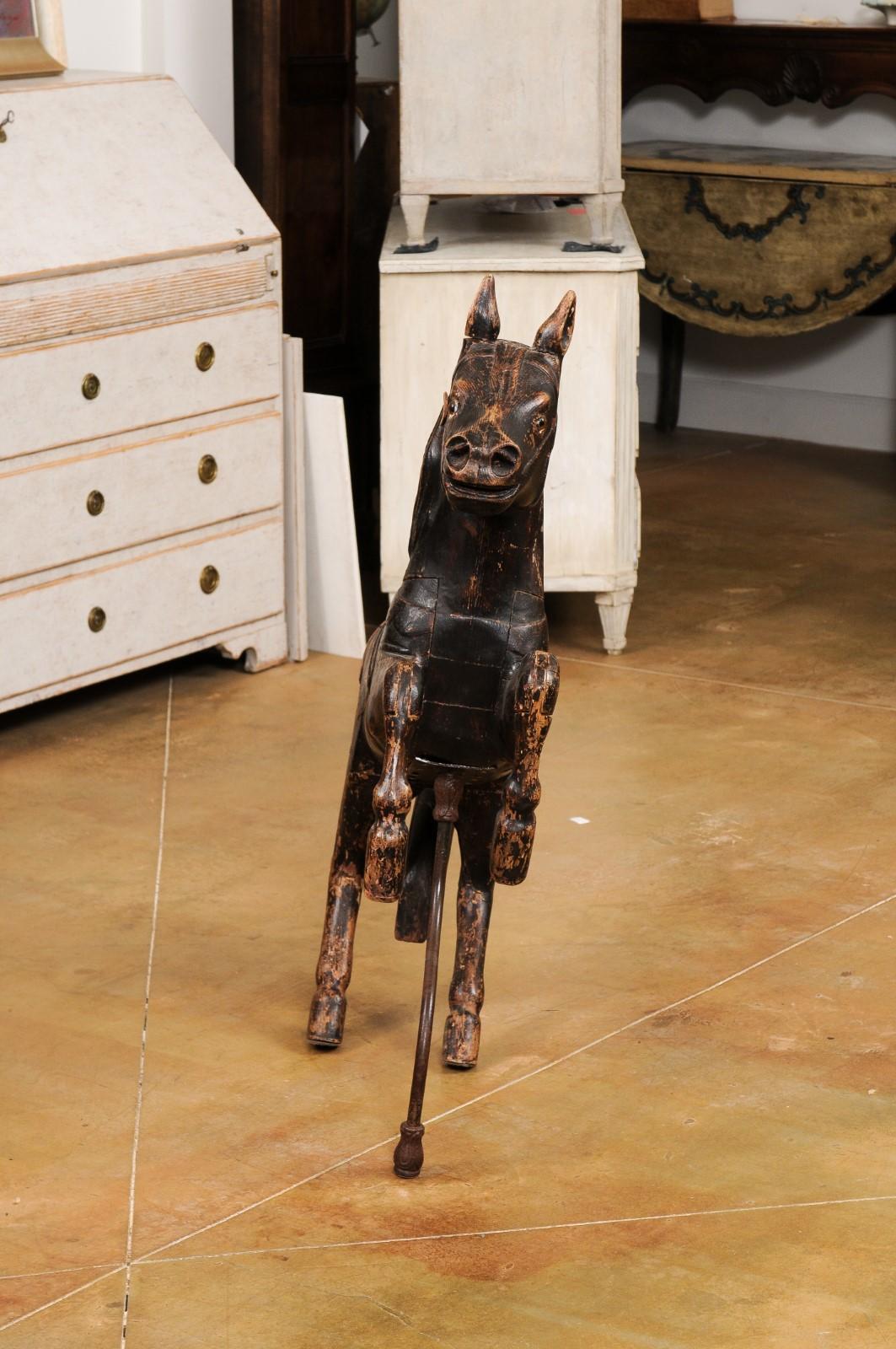 A French carved wooden carousel horse sculpture from the late 19th century, with dark paint, glass eyes, supporting bar and distressed appearance. Created in France during the last quarter of the 19th century, this carved wooden sculpture depicts a