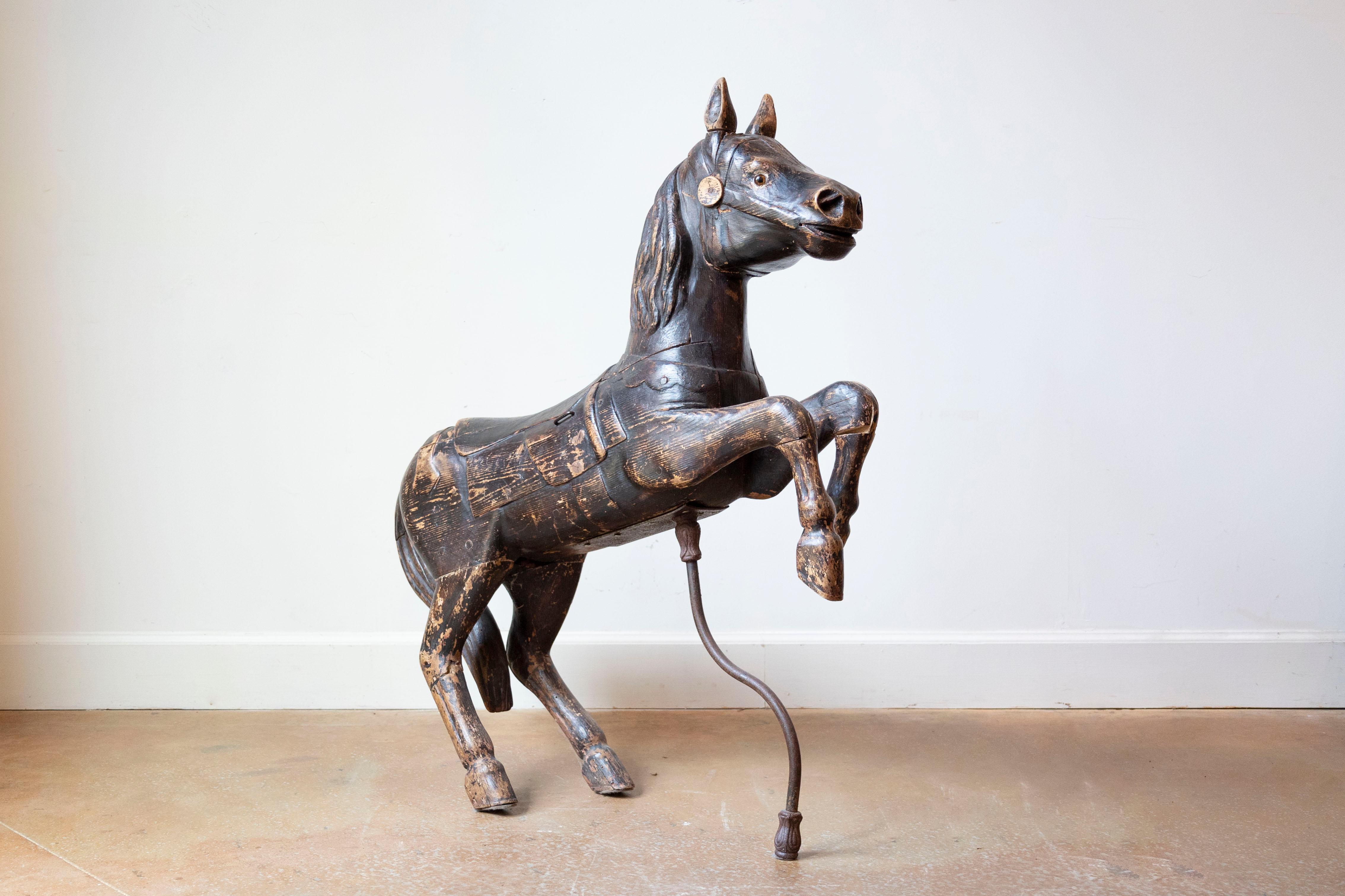 A French carved wooden carousel horse sculpture from the late 19th century, with dark paint, glass eyes, supporting bar and distressed appearance. Created in France during the last quarter of the 19th century, this carved wooden sculpture depicts a