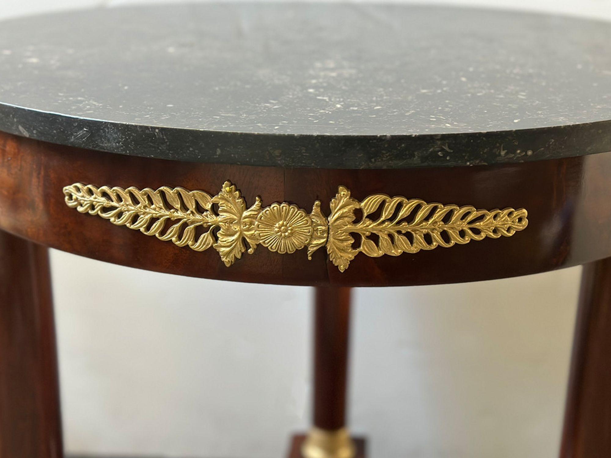 French Late 19th-Century empire style mahogany side table with marble top and bronze accents. Topping this magnificent piece is a round marble surface. The marble's natural veining and luster create a stunning contrast against the rich mahogany
