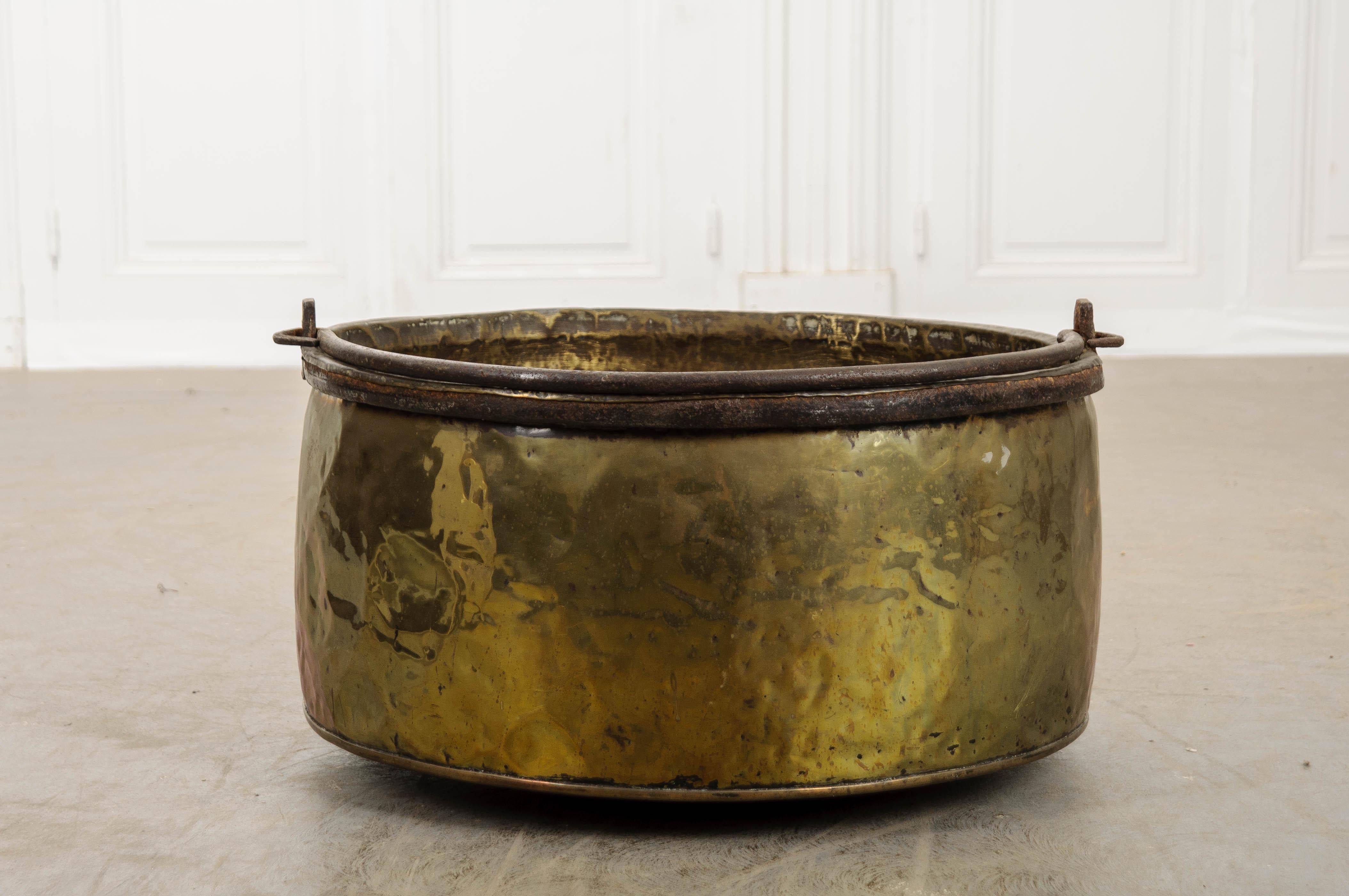 A sizable vessel, made in France circa 1880 of solid brass. The pot has a large iron handle for carrying or hanging it. It will lay flat when not being used. Over the years, the brass has taken on an antiqued character with decades of dings and