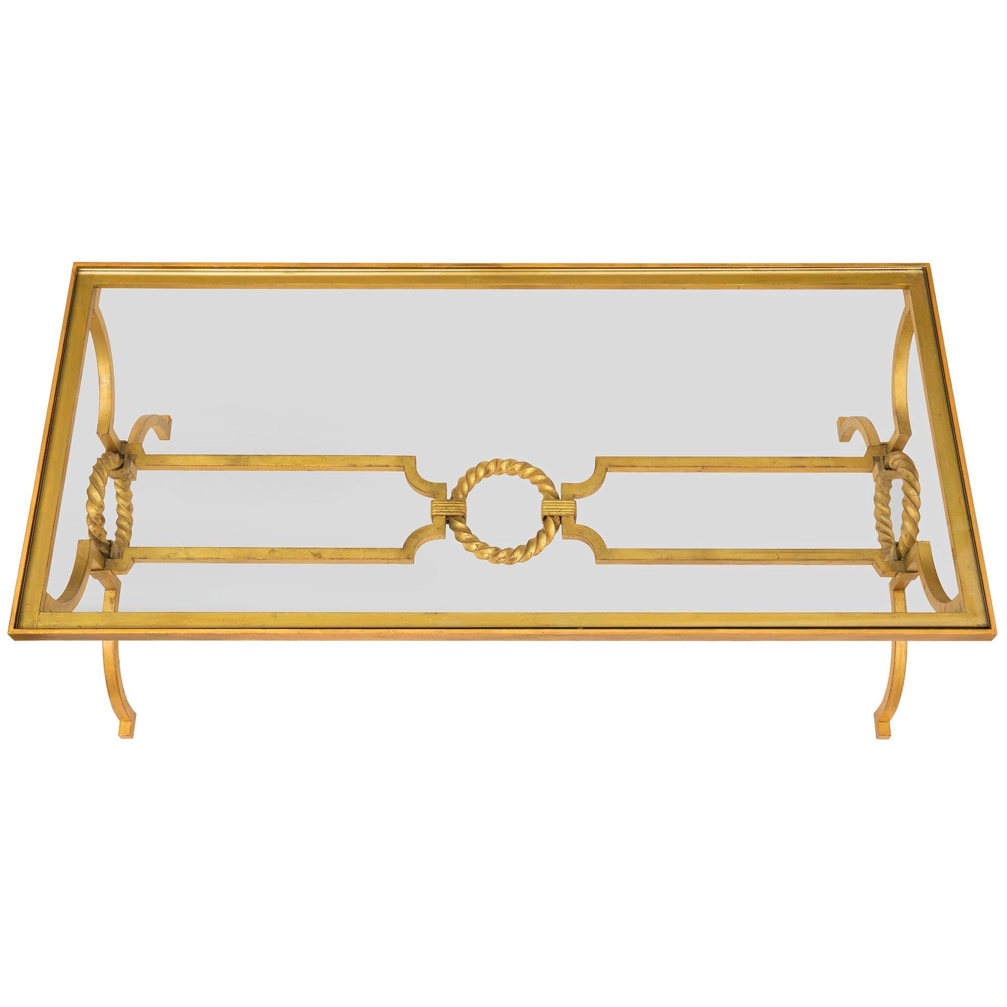 An elegant French late 19th century Louis XVI st. gilt iron and glass coffee table. The table is raised by lovely curved square supports with a superb and most decorative twisted wreath design at each side. The supports are connected by a beautiful
