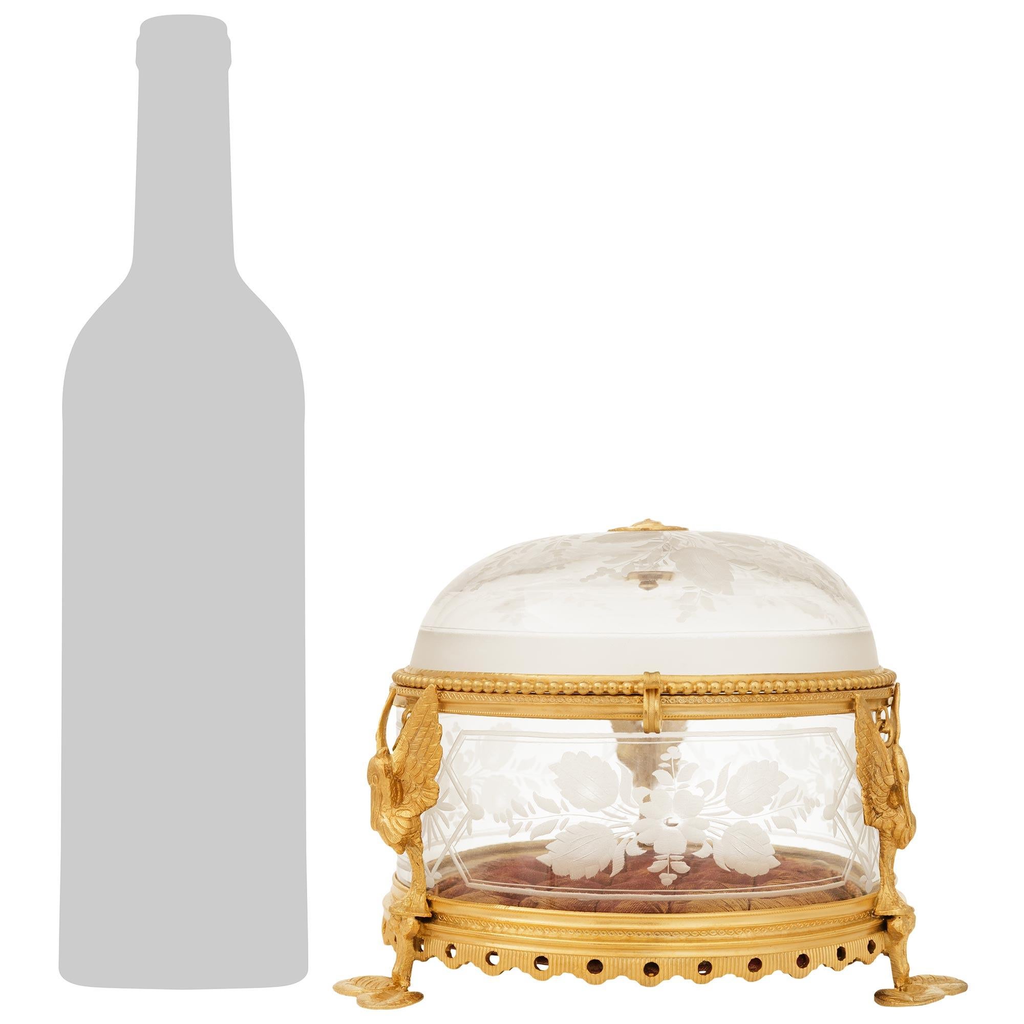 Una caja francesa única y elegantísima de finales del siglo XIX, de estilo Luis XVI, de cristal y ormolu. Esta encantadora caja con tapa de cristal grabado se eleva sobre patas de Ormolu en forma de nenúfares bajo tres pelícanos de alas abiertas. El