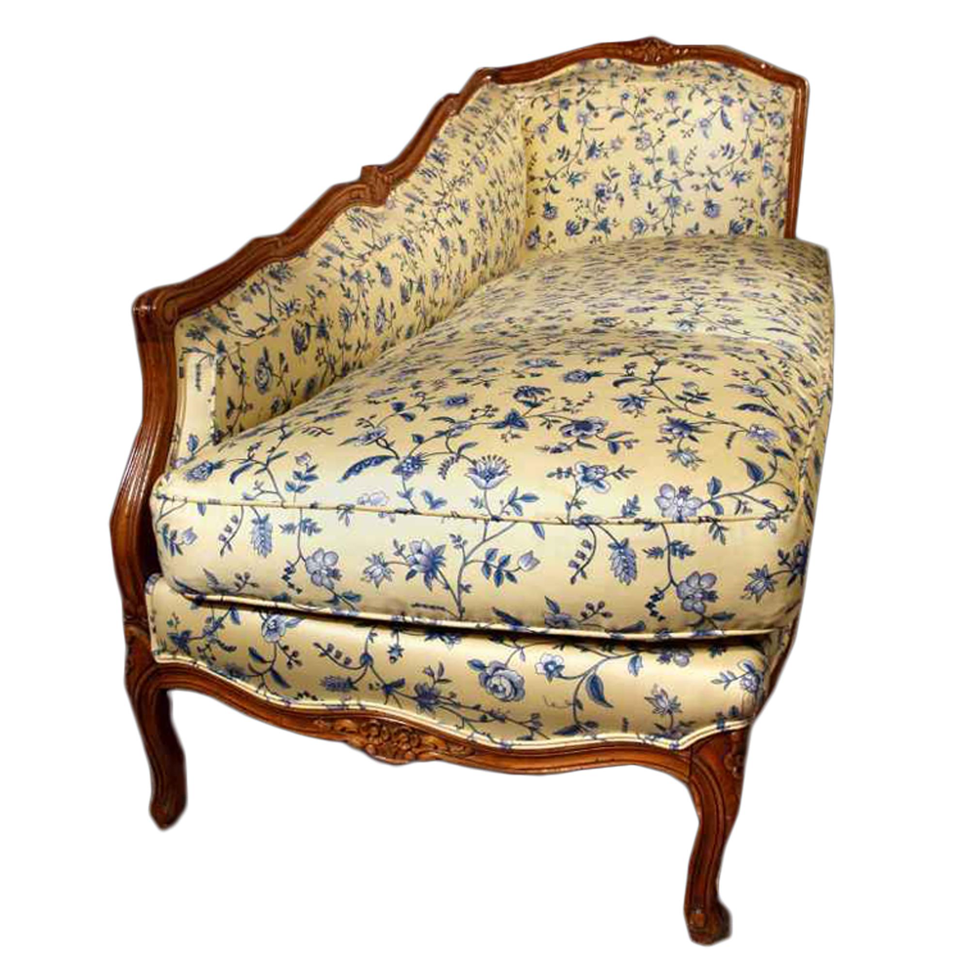 An elegant and unusual country French late 19th century Louis XVI style honey colored oak lounge chair. Upholstered on all sides with a handsome blue and yellow fabric. Raised on six 's' scrolled supports, the lounge chair has a scalloped moulded