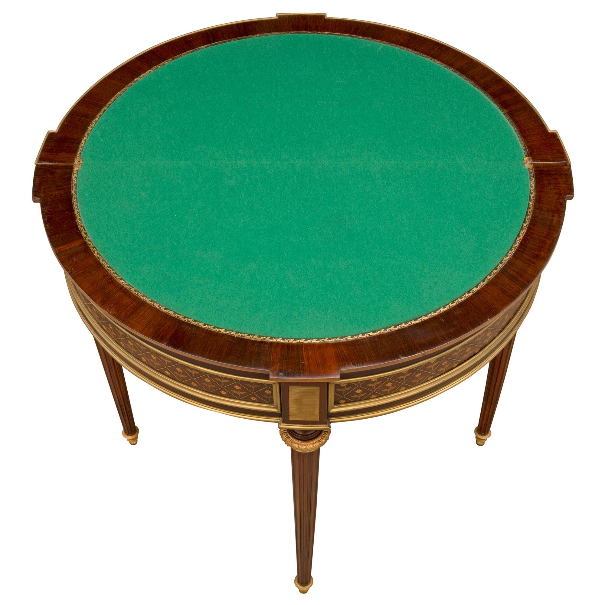 A most elegant French late 19th century Louis XVI st. mahogany, tulipwood, charmwood, and ormolu games table. The table is raised by four circular fluted tapered legs with fine ormolu topie shaped feet and lovely ormolu top caps. Above the front