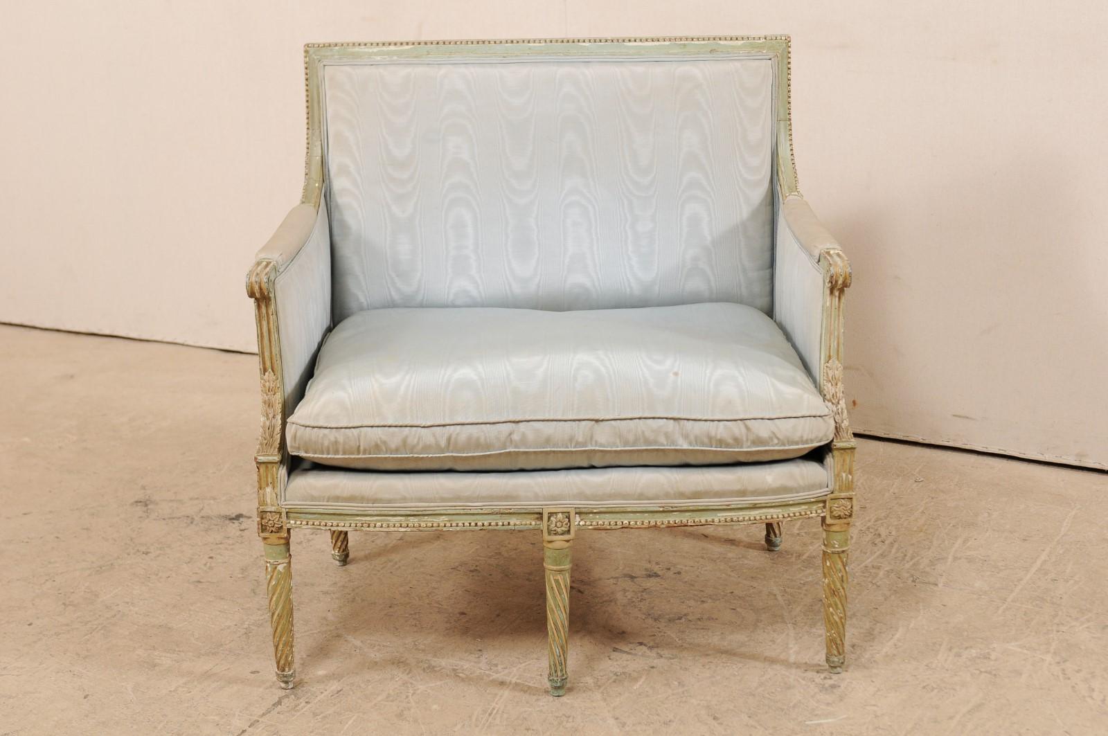 A French Louis XVI style marquise wide seat chair from the late 19th century. This antique Louis XVI style chair from France, with its original paint, features a straight crest rail along the back with carved bead trim, upholstered manchette arms,