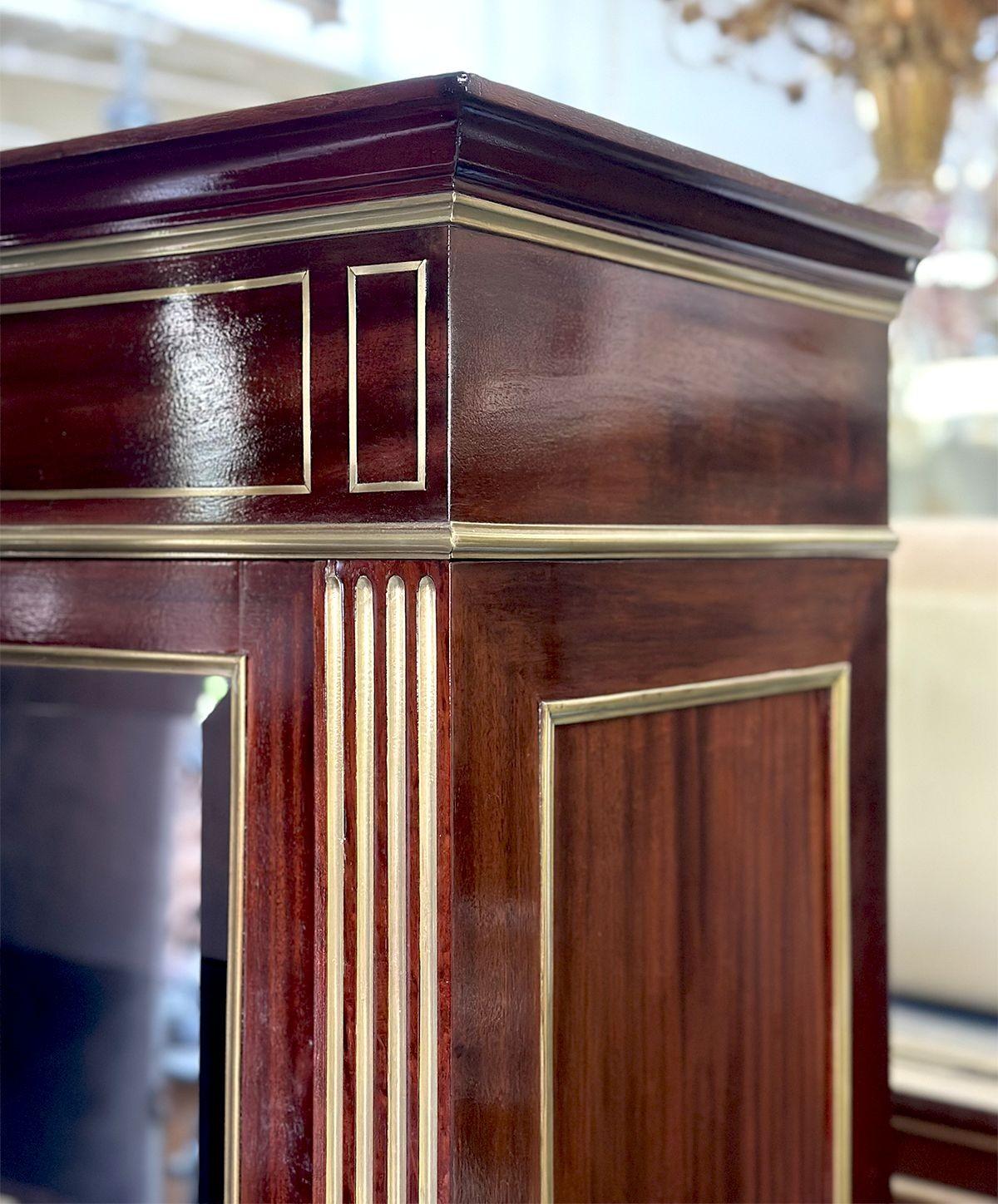 Una tradizionale vetrinetta realizzata in Francia alla fine del XIX secolo, con una ricca cornice in mogano e finiture intarsiate in ottone su tutto il perimetro e ante in vetro smussato. Le porte sono dotate di serratura e chiave per garantire una