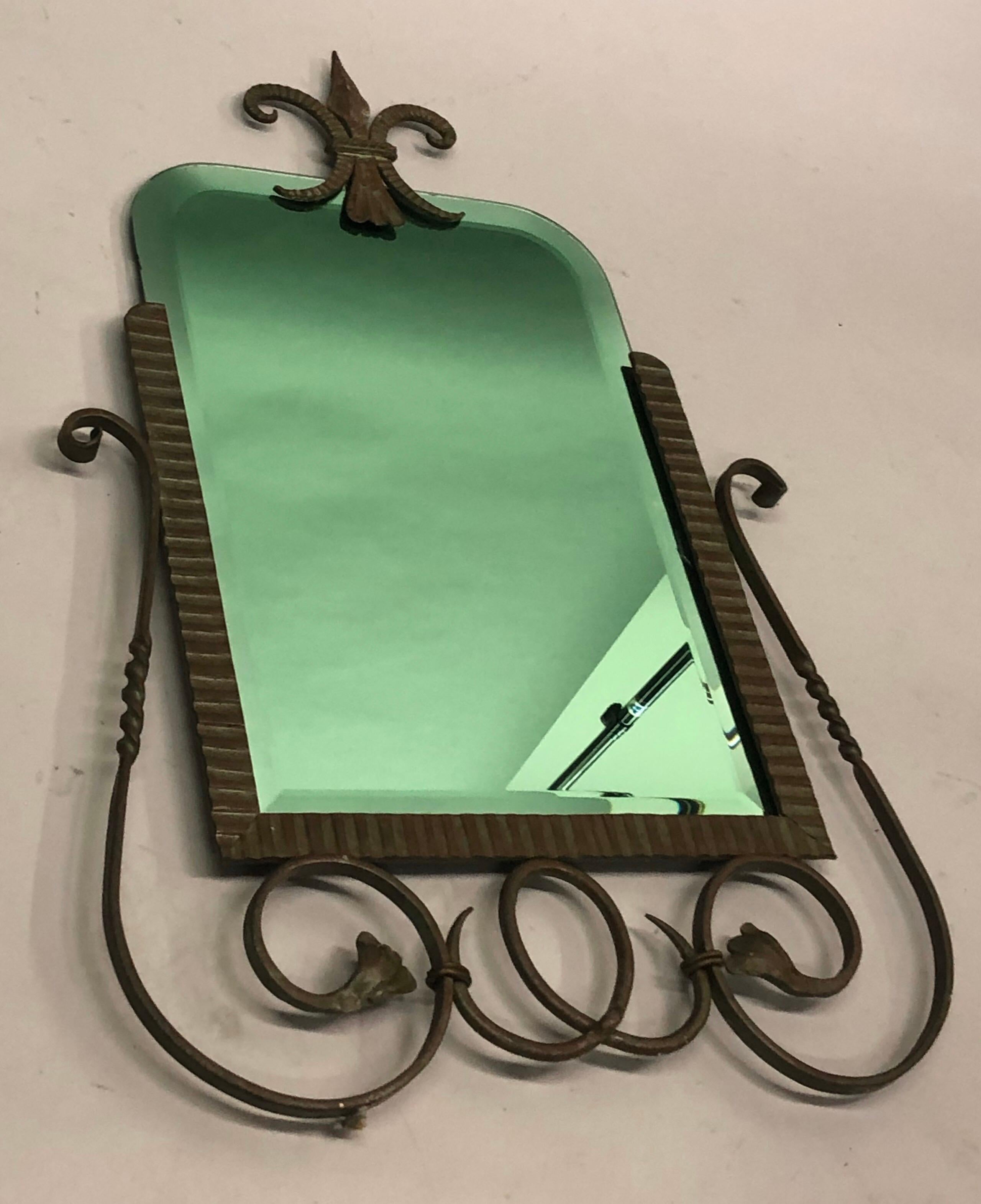 Elegante specchio francese in ferro e bronzo lavorato e martellato a mano con uno straordinario e raro specchio con inserto in vetro verde alla maniera di Gilbert Poillerat.  Il pezzo è completato da uno stemma in bronzo a forma di fiore d'angelo