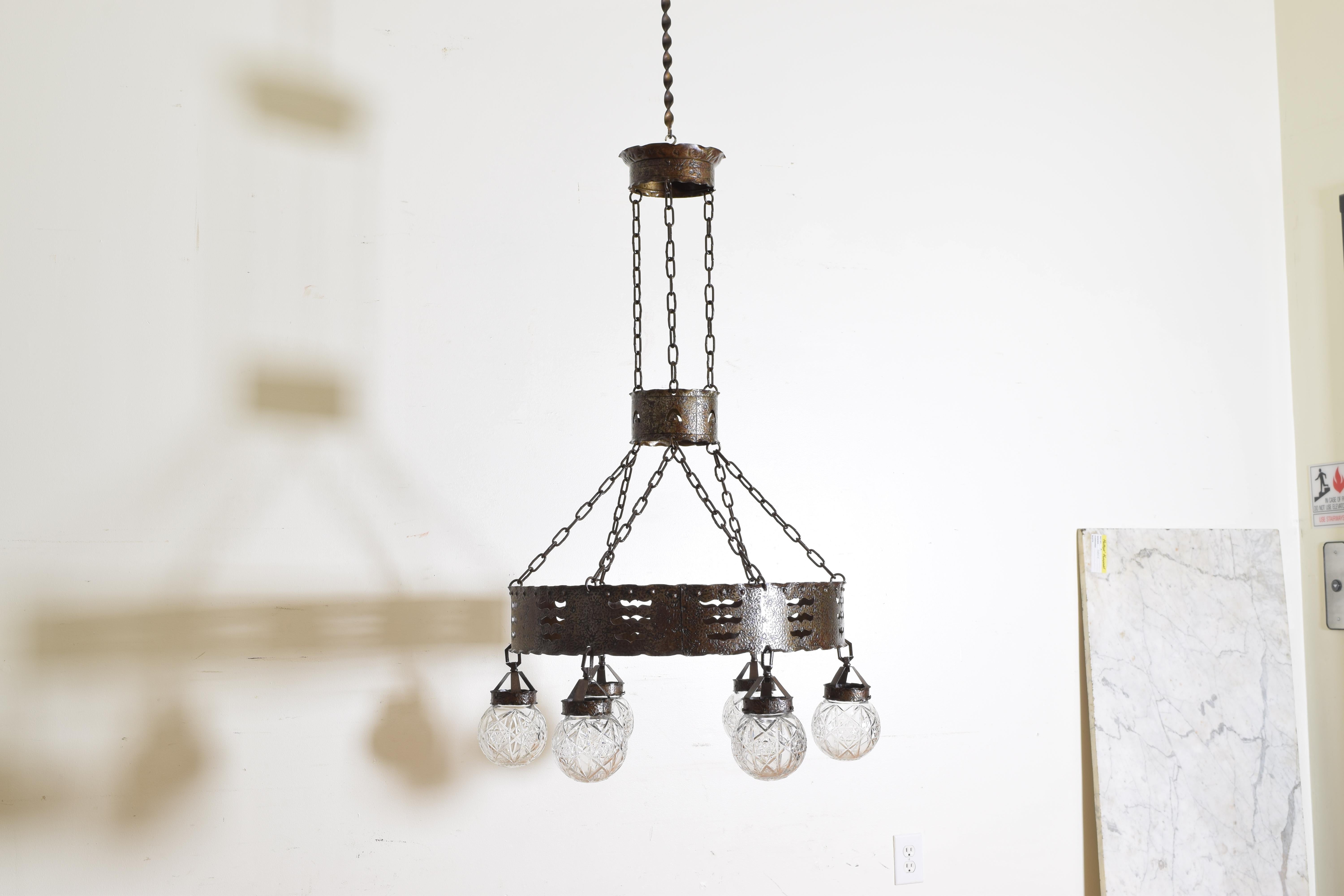 Hanging from a crowned cylinder top with original chains connecting to a middle cylinder and then double chains connecting to the main ring which is perforated with wave patterns, all the steel elements hammered and etched, with six cut glass globes