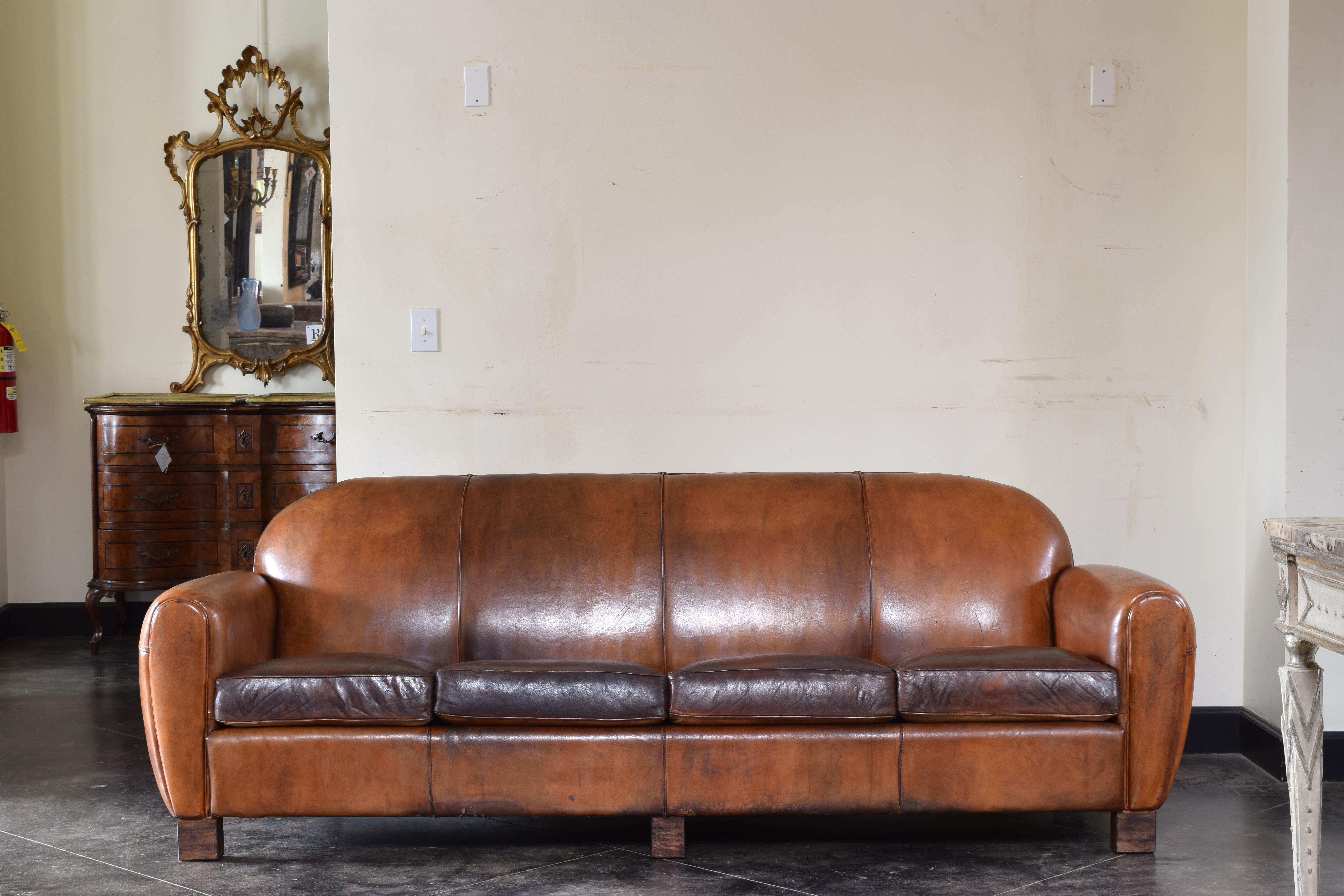 Having a slightly arched backrest with upholstered arms and four down cushions with leather piping throughout, raised on block feet, nearly perfect condition, the cushions recently refreshed.