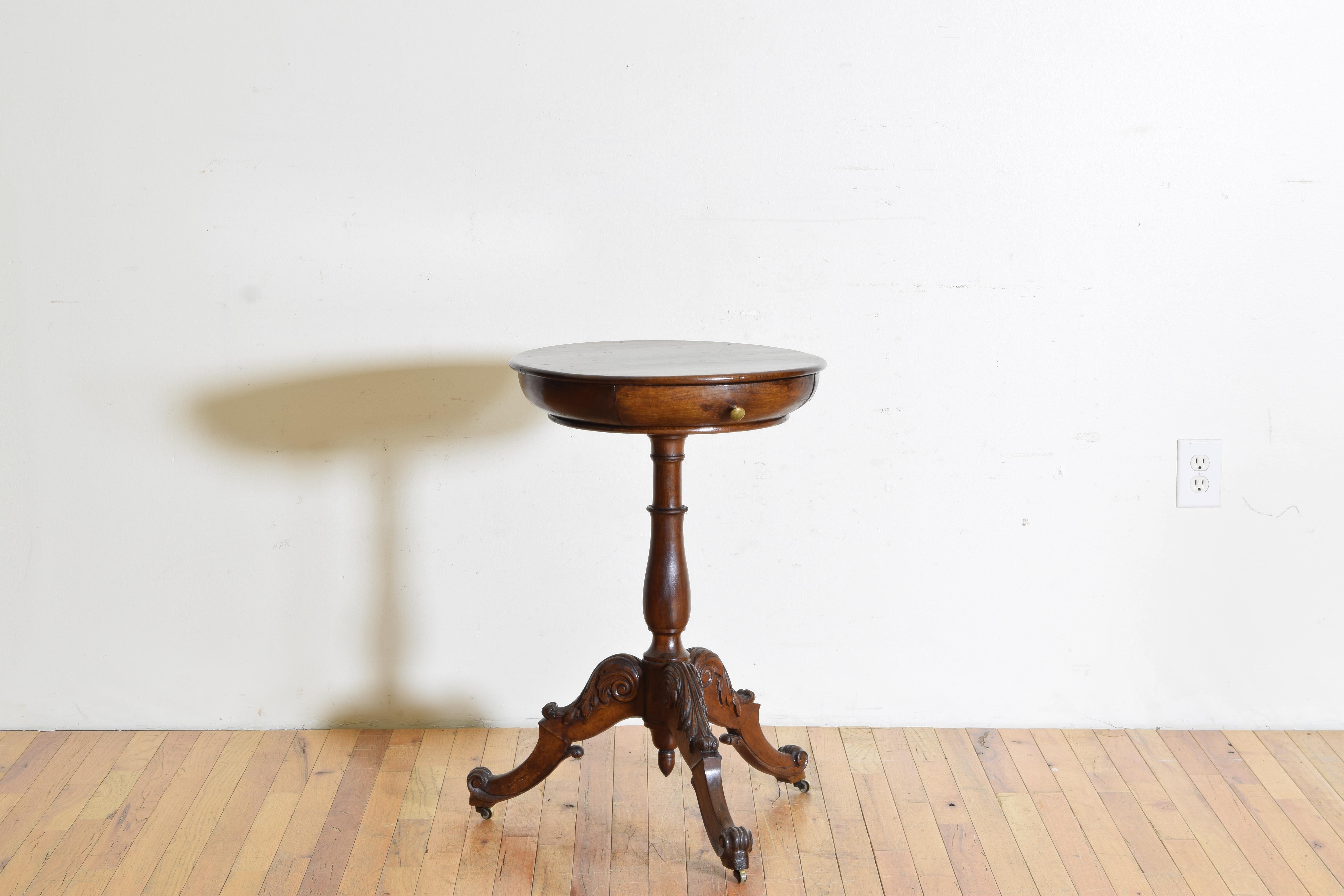 having a circular top of curved, almost bowl-like, design houisng one drawer, raised on a turned standard issuing three carved legs terminating in brass casters, with shaped central terminal.