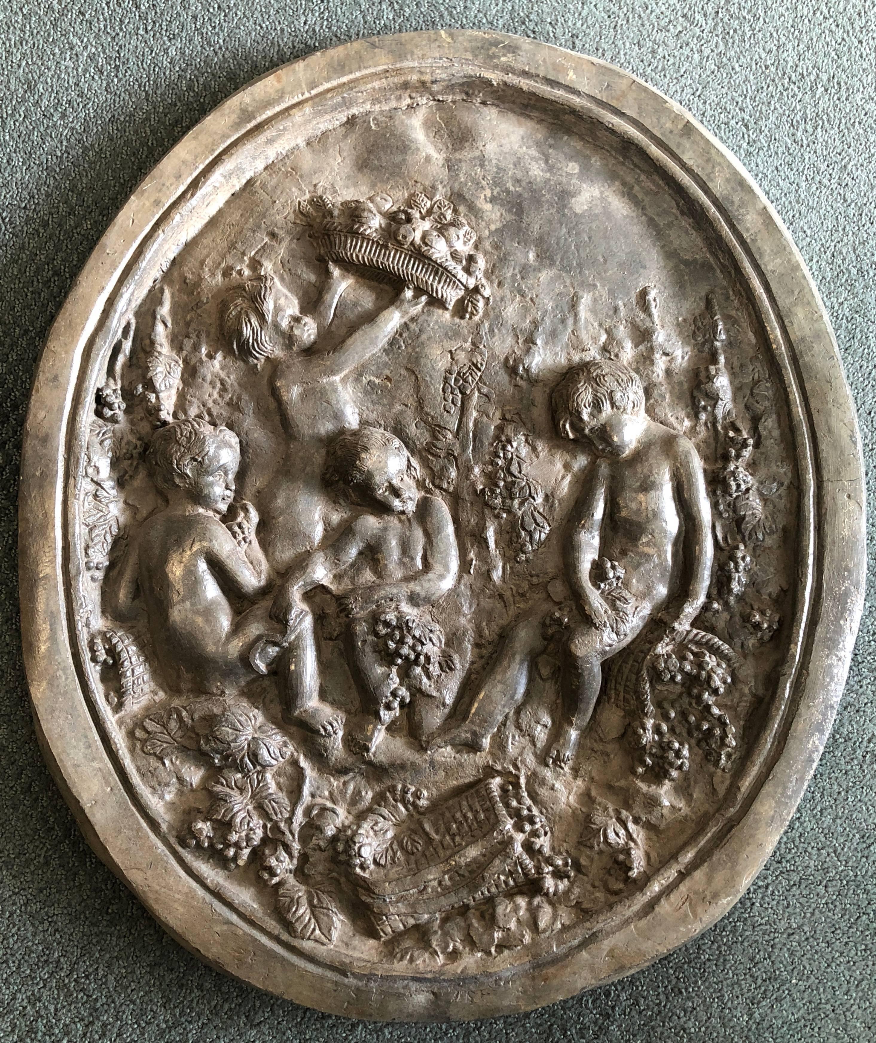 Oval lead plaque moulded in high relief with a scene of cherubs, gathering grapes and fruit. 
Probably French, 18th century

Very suitable to wall mount as a garden accent.