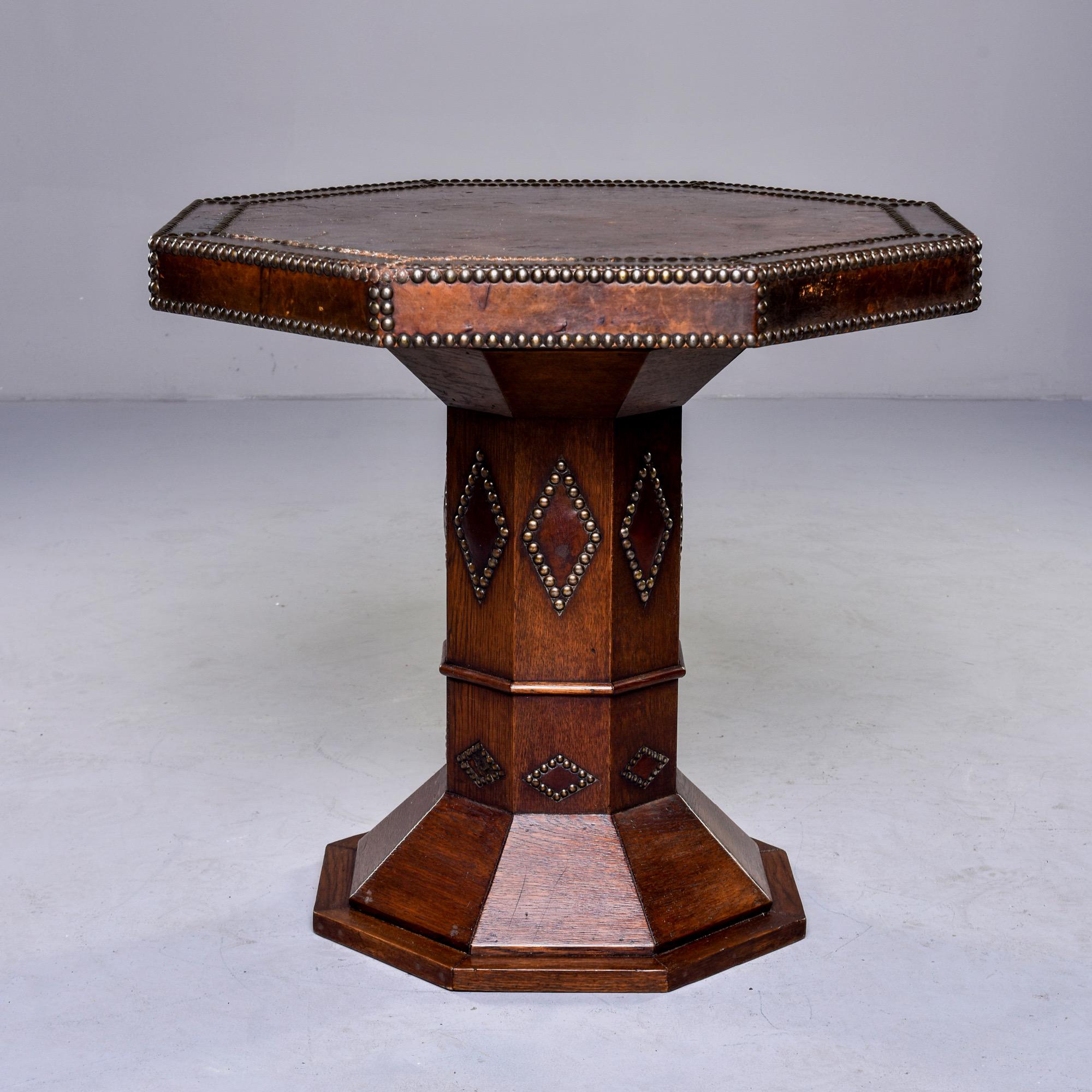 Circa 1930s French Art Deco oak side table features and eight sided top covered in leather with decorative brass nail head studs. Pedestal base has eight panels as well and center support is decorated with brass nail heads in diamond patterns.