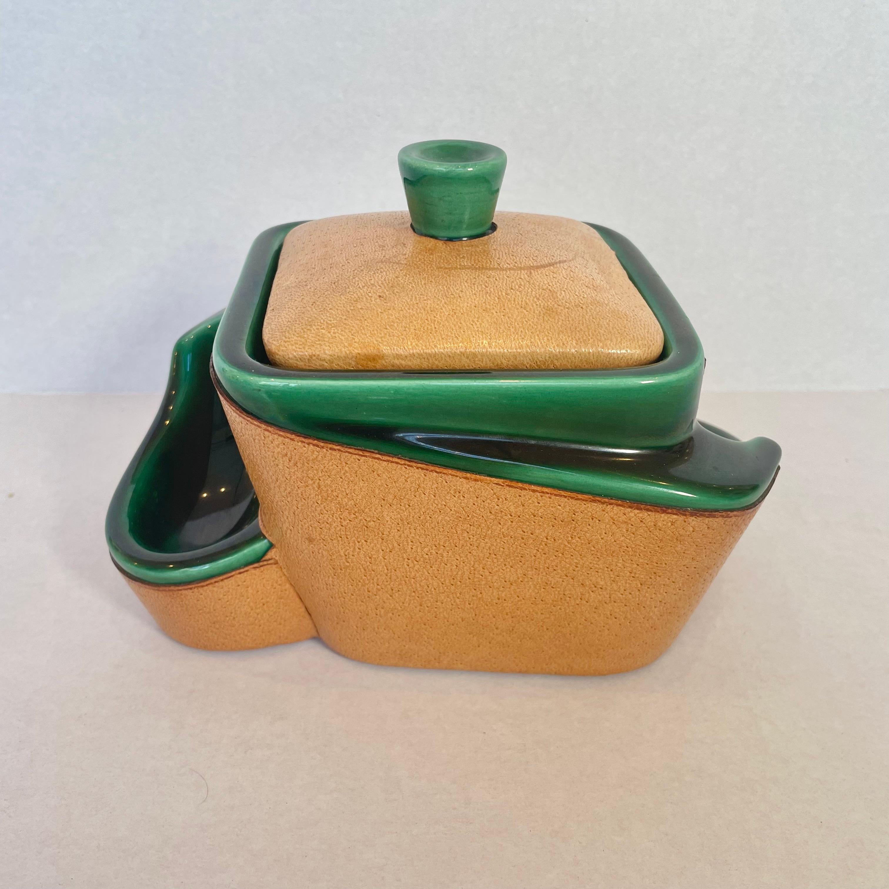 Handsome leather and ceramic tobacco/weed jar and pipe holder. Beautiful green ceramic and perfect patina to tan leather with a felted base. Opens up to reveal the stash jar while the sides are shaped to hold pipes or ashes from cigarettes. Great