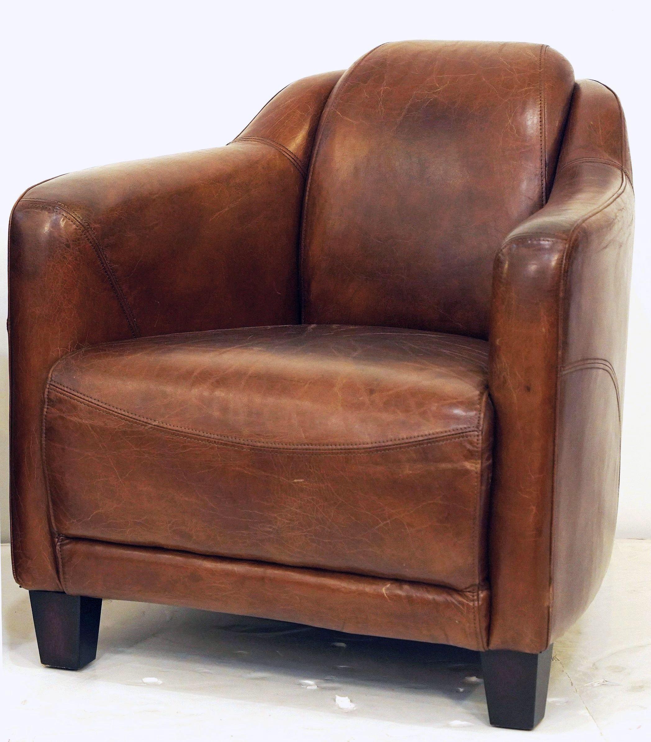 A handsome and comfortable French club or aviator lounge chair upholstered in a cognac or tobacco brown leather - featuring Art Deco styling in the rounded sides and curved arms - and Jazz-era club chair design in the stitched leather back and