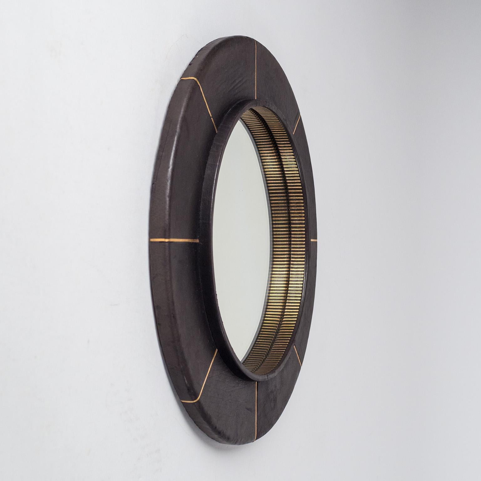 French leather-clad mirror, circa 1980, with gold-embossed decorations. Black anilin leather with radial gold lines embossed into the leather. Good condition with minor wear to the leather and some clouding on the mirror. Reflective area is