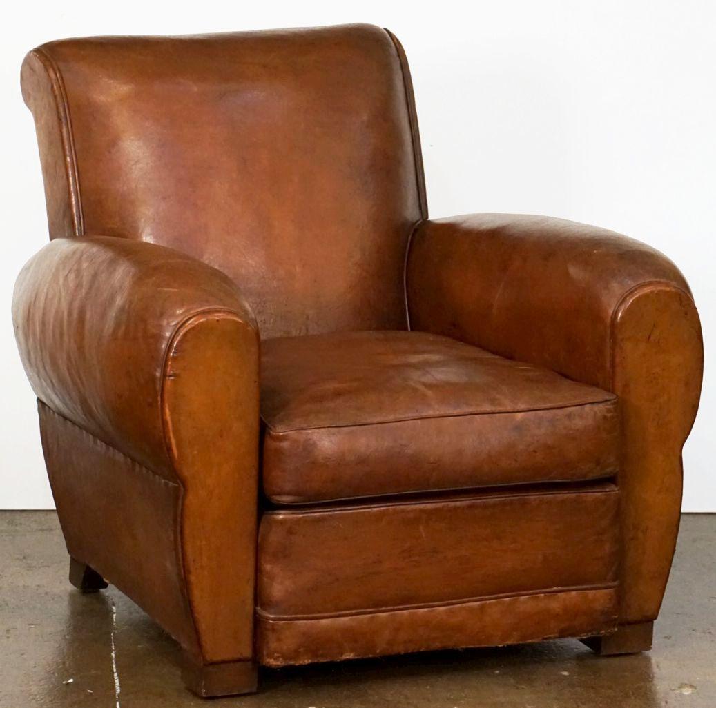 A handsome vintage French leather upholstered club or lounge chair from the Art Deco era - featuring a comfortable back and seat with removable cushion, with stylish arms and original leather, brass nail-head trim to back, and resting on block
