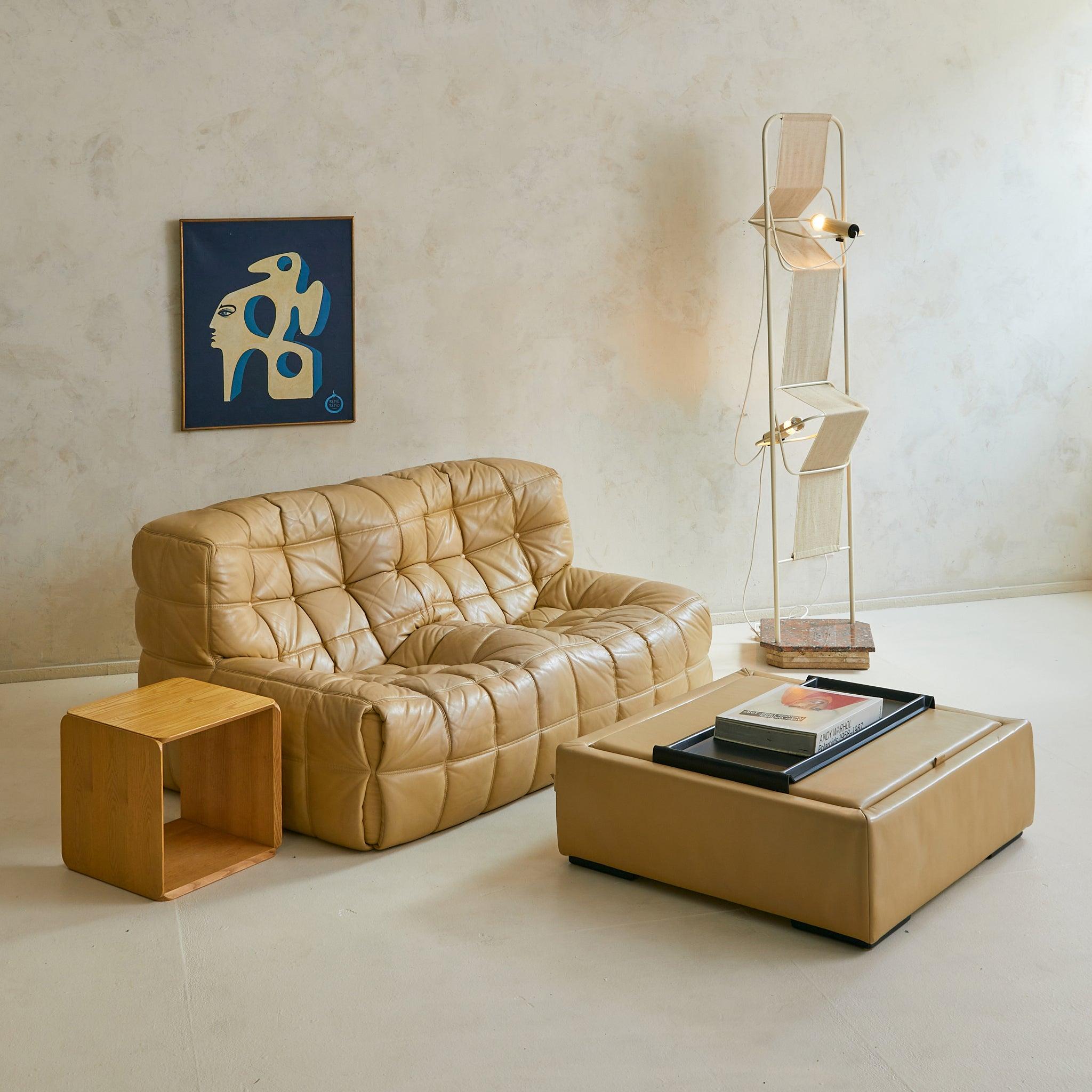 A rare 1970s coffee table by Ligne Roset, France. Wrapped in supple ecru-toned leather, the low square form is softly padded at the sides with four recessed legs. The hinged top lifts to reveal a lined storage well, while a charcoal-toned tray rests