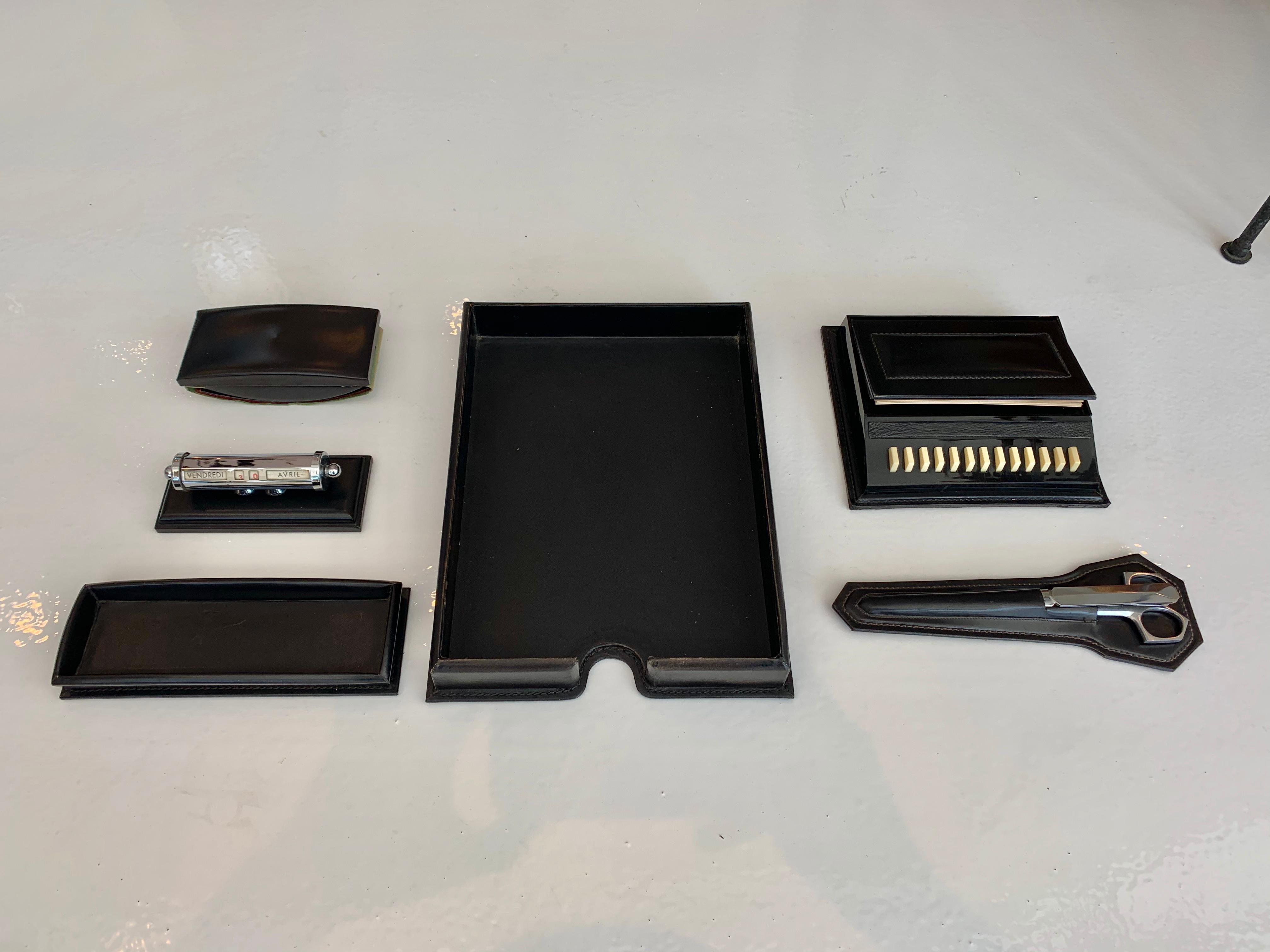 Fantastic 6 piece French leather desk set by Le Tanneur. All pieces wrapped in black leather with white contrast stitching. Desk set features a paper holder, pen holder, ink blotter, adjustable calendar, chrome scissors and letter opener and manual