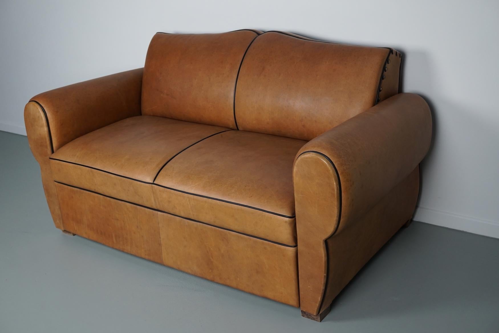 This moustache back club sofa was made around the 1940s in France. It was reupholstered some years ago with high quality cognac leather with black piping and the springs / foam was changed for a firmer seat.