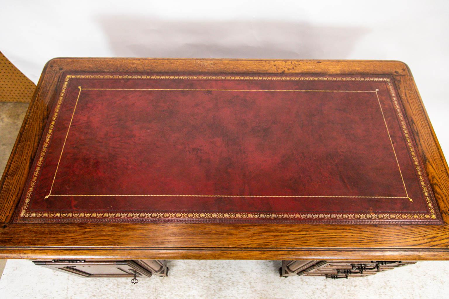 This French leather top desk is finished with shaped raised panels on the back and the sides. The hardware is original. There is exposed double peg construction on the top and front. The leather top is a burgundy with gold detailing around the edges.