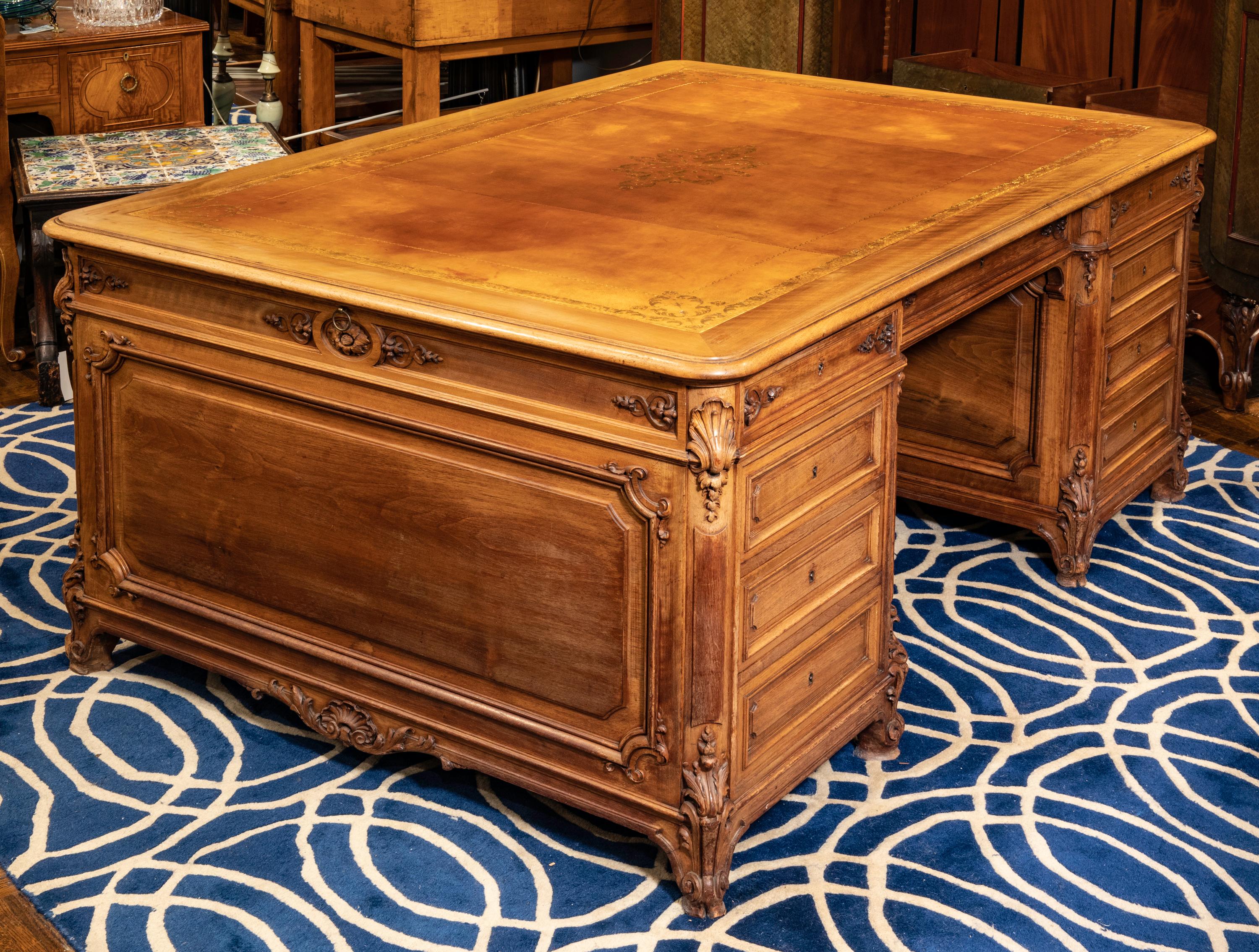 Beautiful 1900s French Louis XV style partner's desk. Very finely carved French oakwood. Leather top in Gilt tooling and glass top for protection. Pencil drawers between banks of four drawers on each sides that extend to the other sides, individual