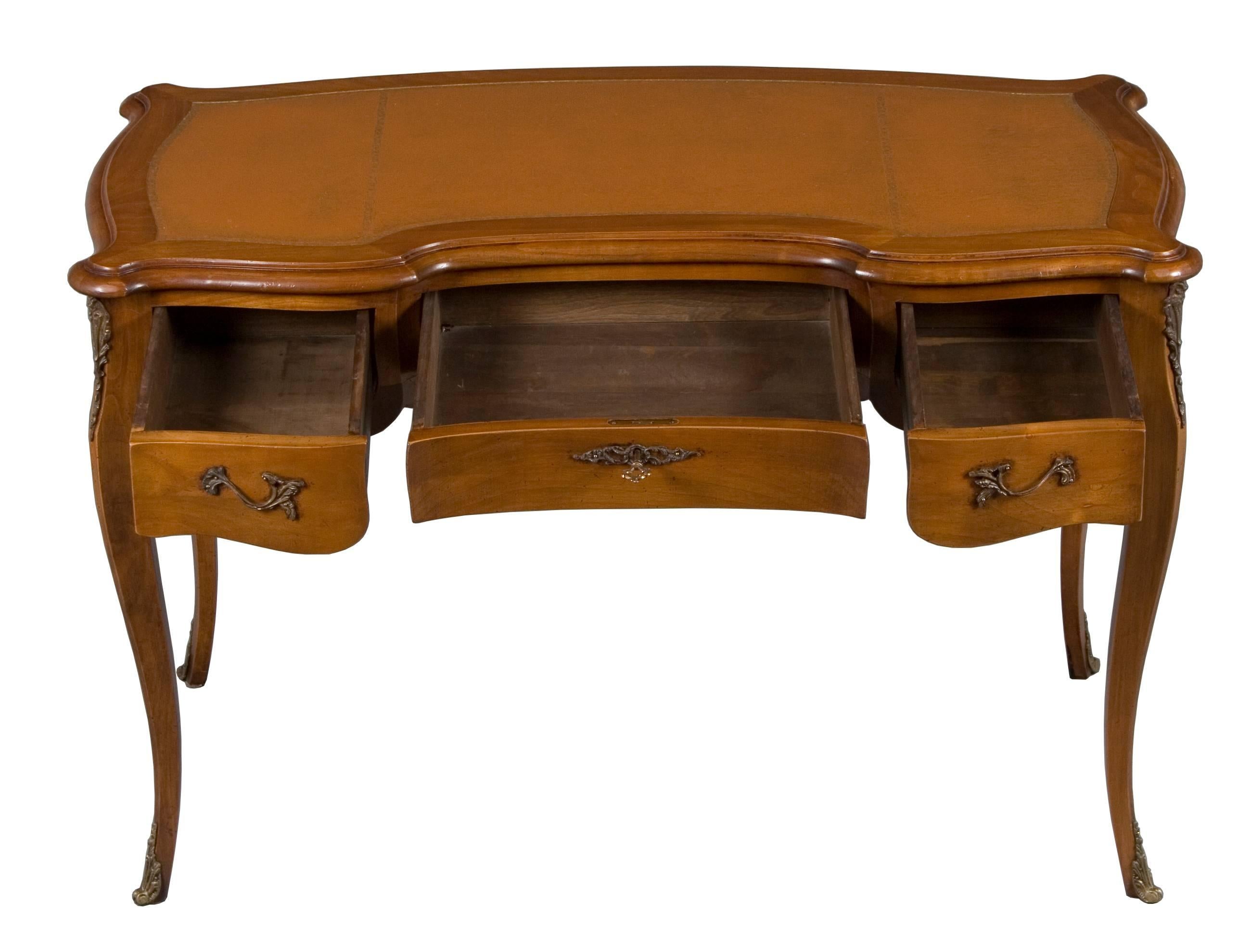 This antique desk hails from France where it was created around the year 1900. Done in a Louis XV style, it makes a wonderful piece to sit at.
This piece consists of carved cherry wood. It retains a stunning patina and medium color. Ormolu mounted
