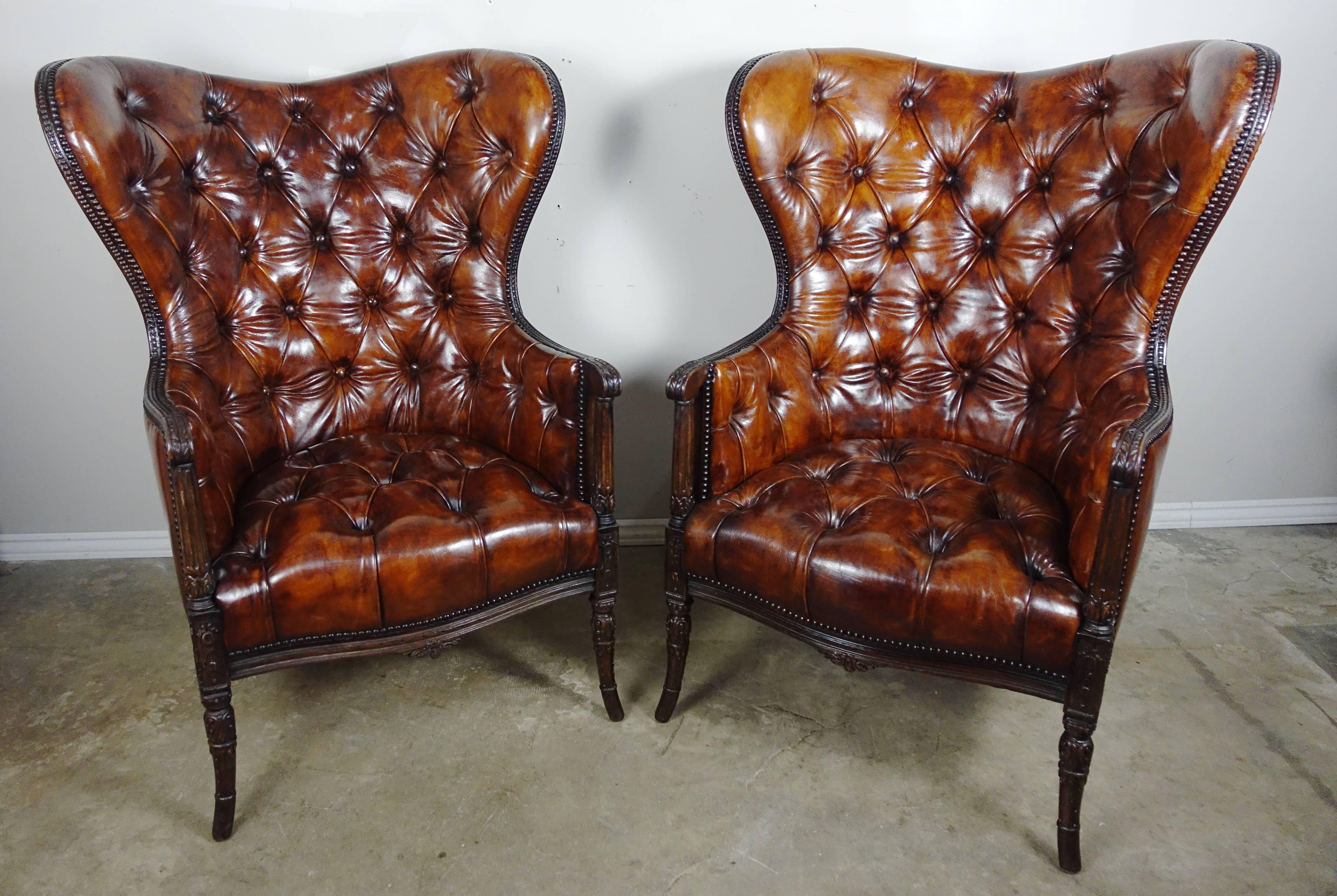 Pair of French wingback rich cognac colored leather tufted armchairs standing on four tapered carved legs. Brass nailhead trim detail.