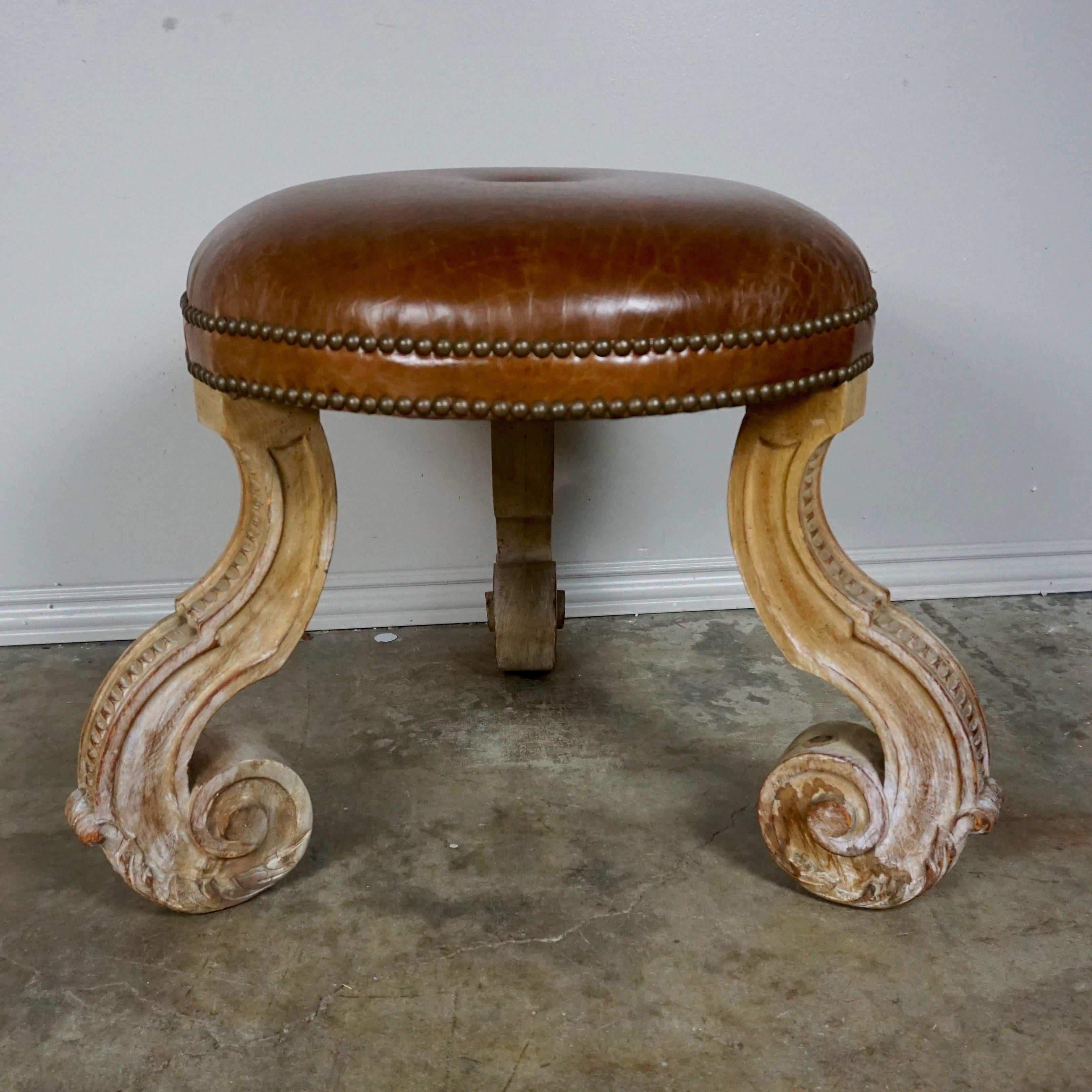 1930s carved wood French tripod stool upholstered in leather with nailhead trim detail.