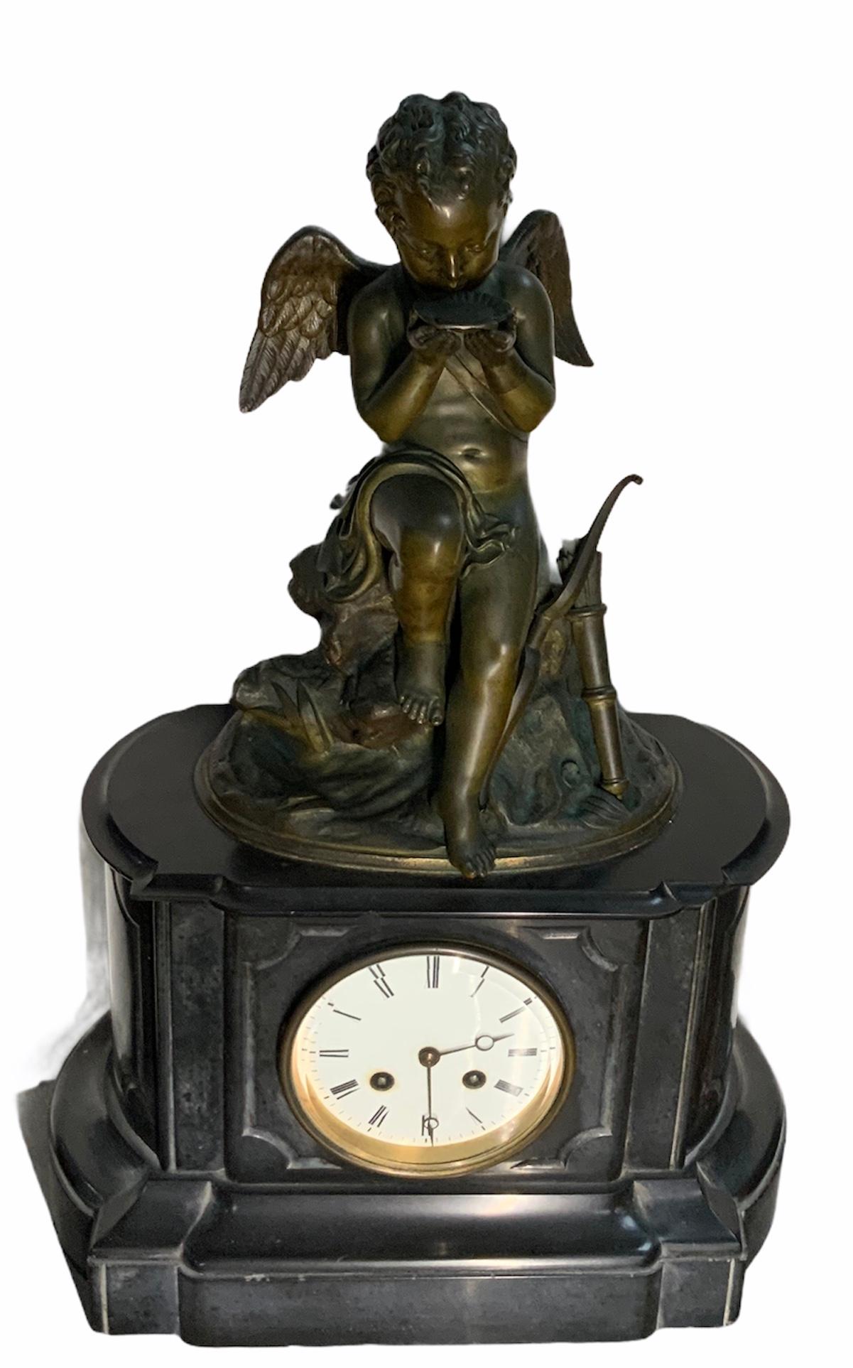 This is a French figural patinated bronze sculpture mantel clock of a winged Cherub hunter by Lemire Charles Gabriel Sauvage. The thirsty Cherub is seated over a large rock with some foliages drinking water from a seashell. He is semi nude and a