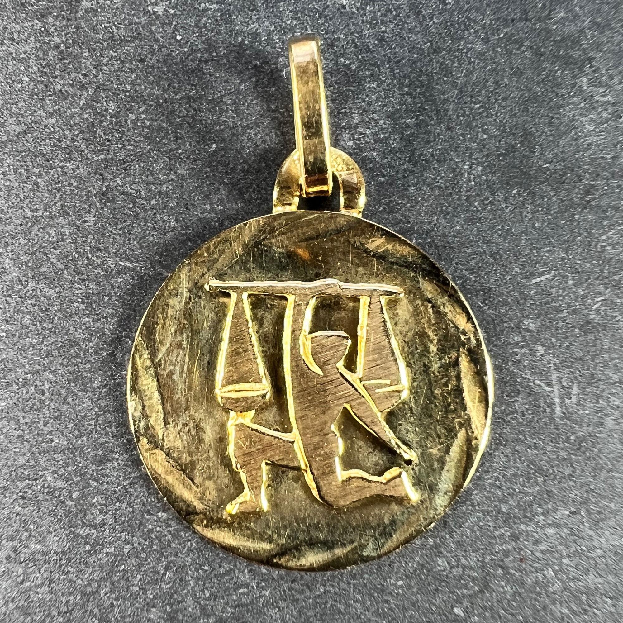 An 18 karat (18K) yellow gold charm pendant designed as the Zodiac sign of Libra, depicting a figure holding a set of balance scales aloft. Stamped with the eagle mark for 18 karat gold and French manufacture with an unknown makers