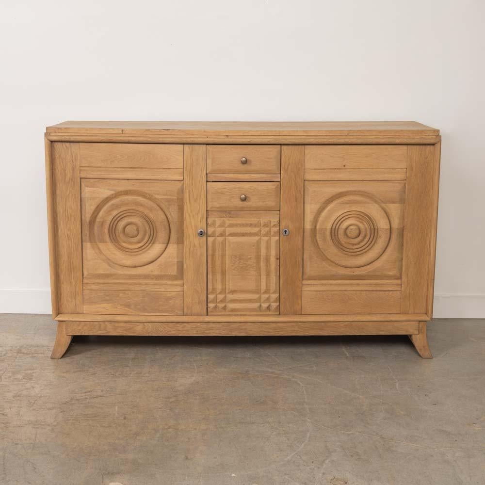 Splendida credenza in rovere chiaro di Charles Dudouyt, proveniente dalla Francia, anni '40. Dettaglio circolare intagliato su due ante con un ripiano interno. Due cassetti centrali per riporre gli oggetti. Poggia su due gambe affusolate intagliate.
