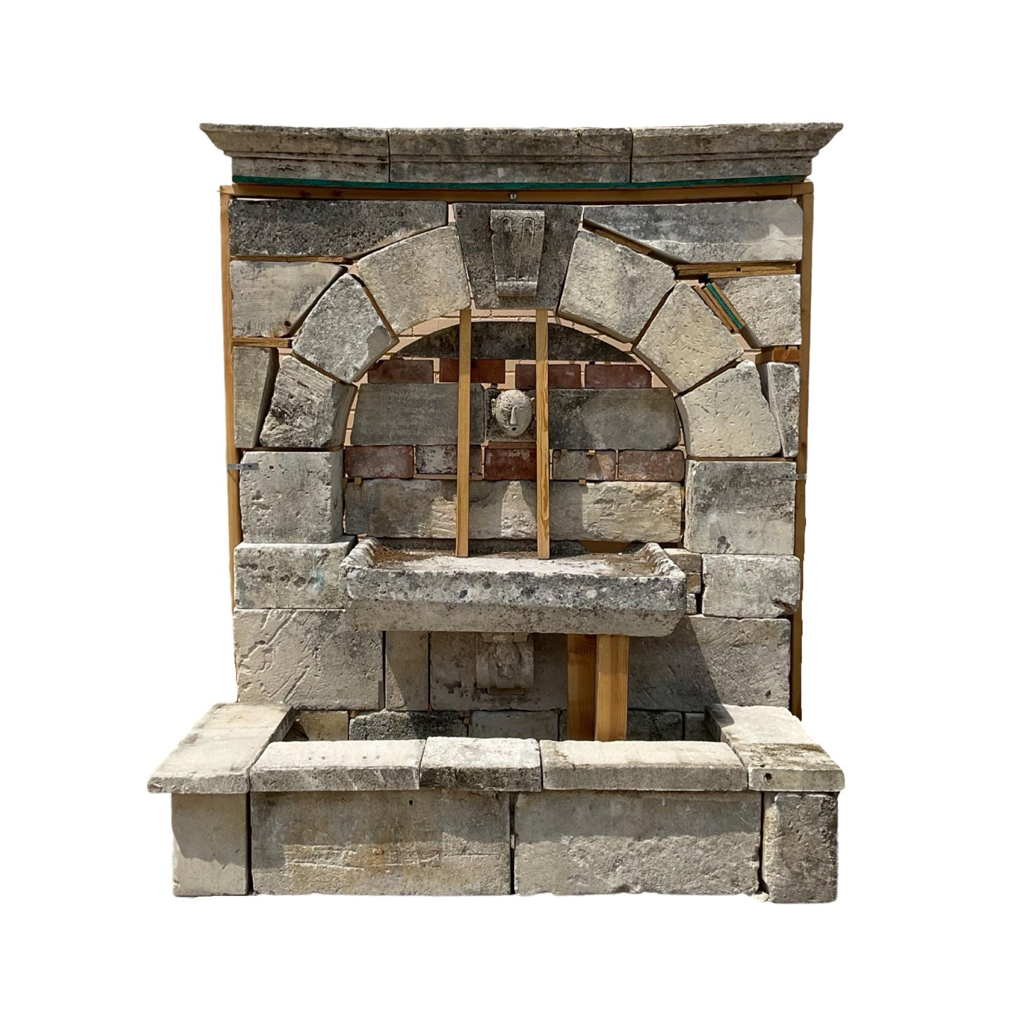 This French Limestone Wall Fountain from the 17th century is a stunning piece of craftsmanship. The antique fountain is made out of limestone, with a carved face sculpture in the center that serves as a water spout exit and a middle trough basin for